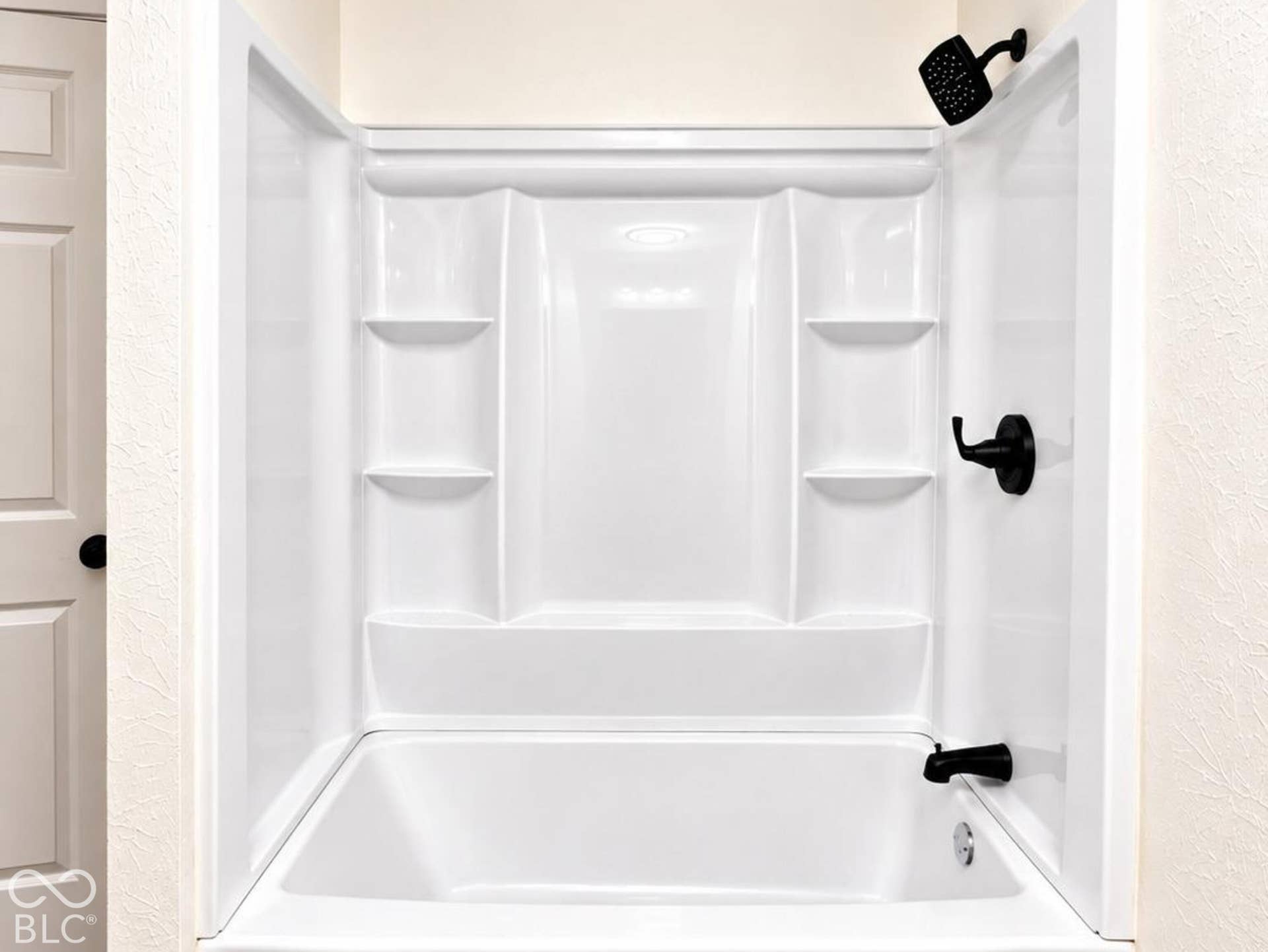 White shower-tub combination featuring integrated shelving, matte black fixtures, and wood-finish flooring