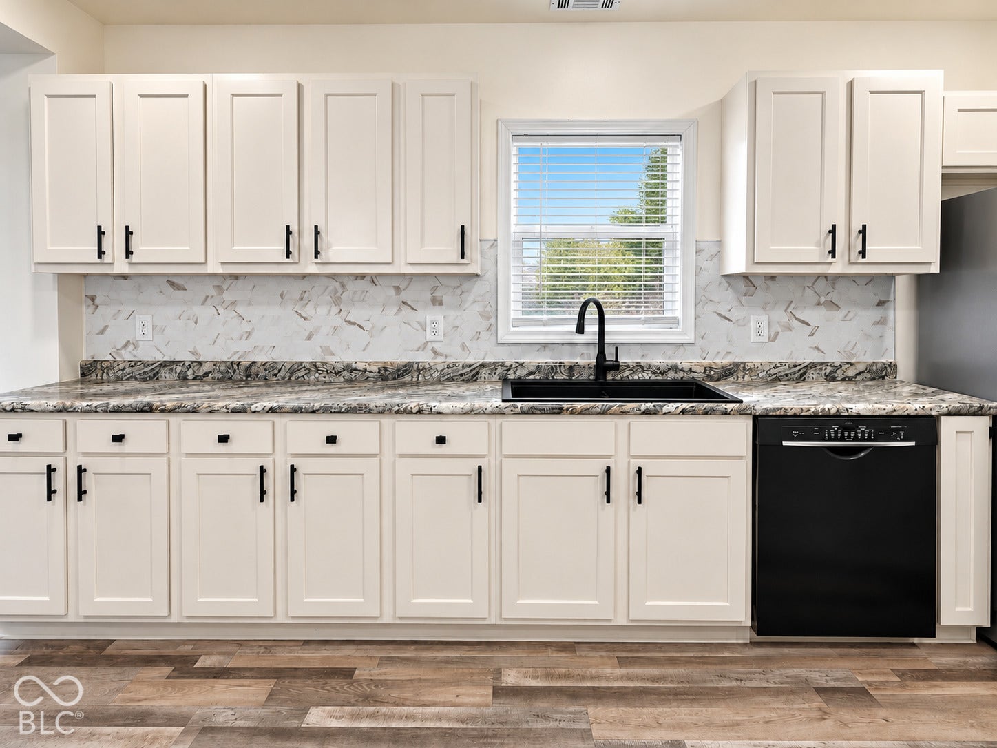 Kitchen featuring white shaker-style cabinetry, patterned stone-finish countertops, full-height decorative backsplash, matte black hardware, and an integrated undermount sink with a high-arch faucet