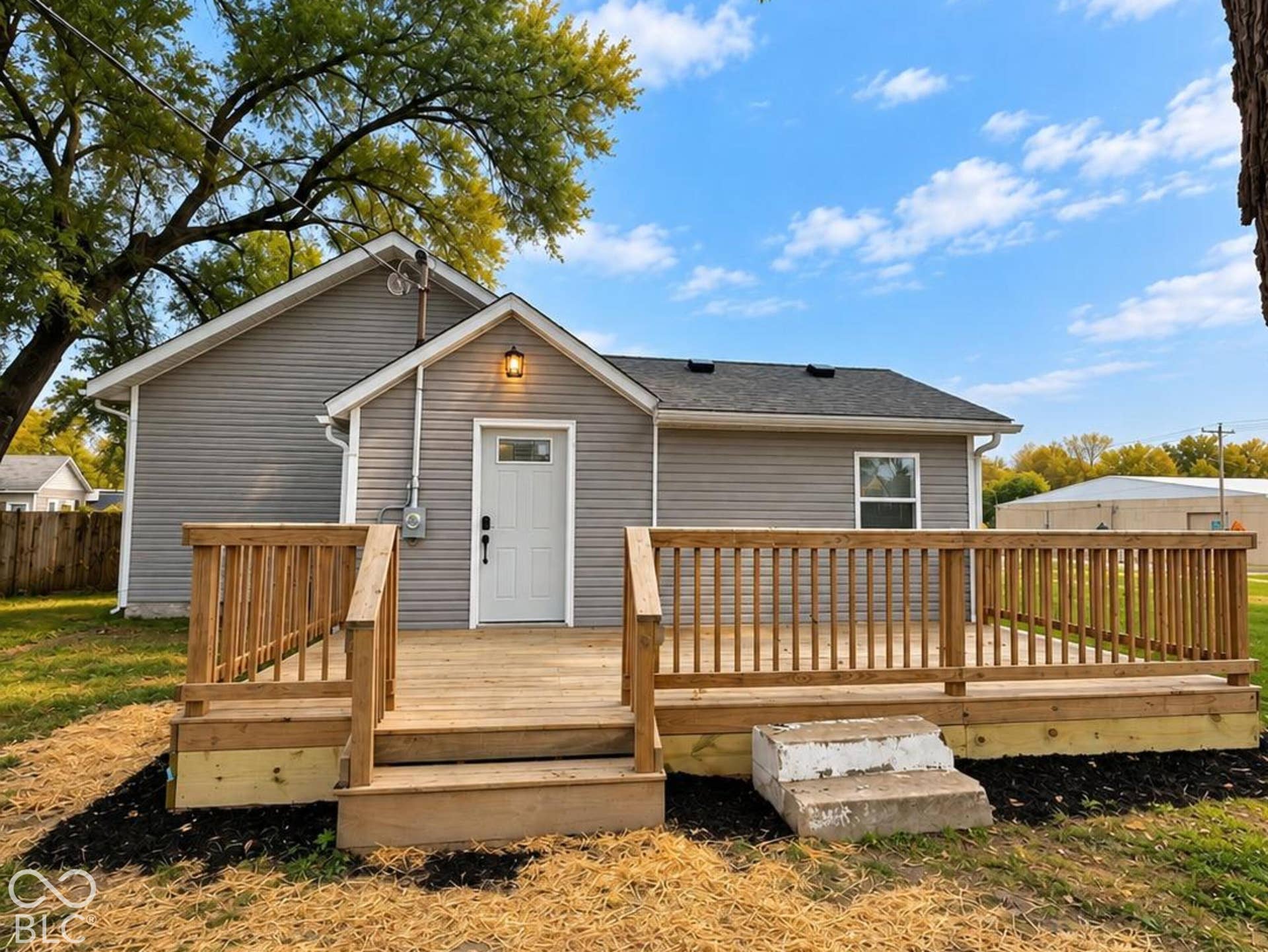 Exterior view featuring gray horizontal siding, a wood deck with railings, and an attached exterior light fixture