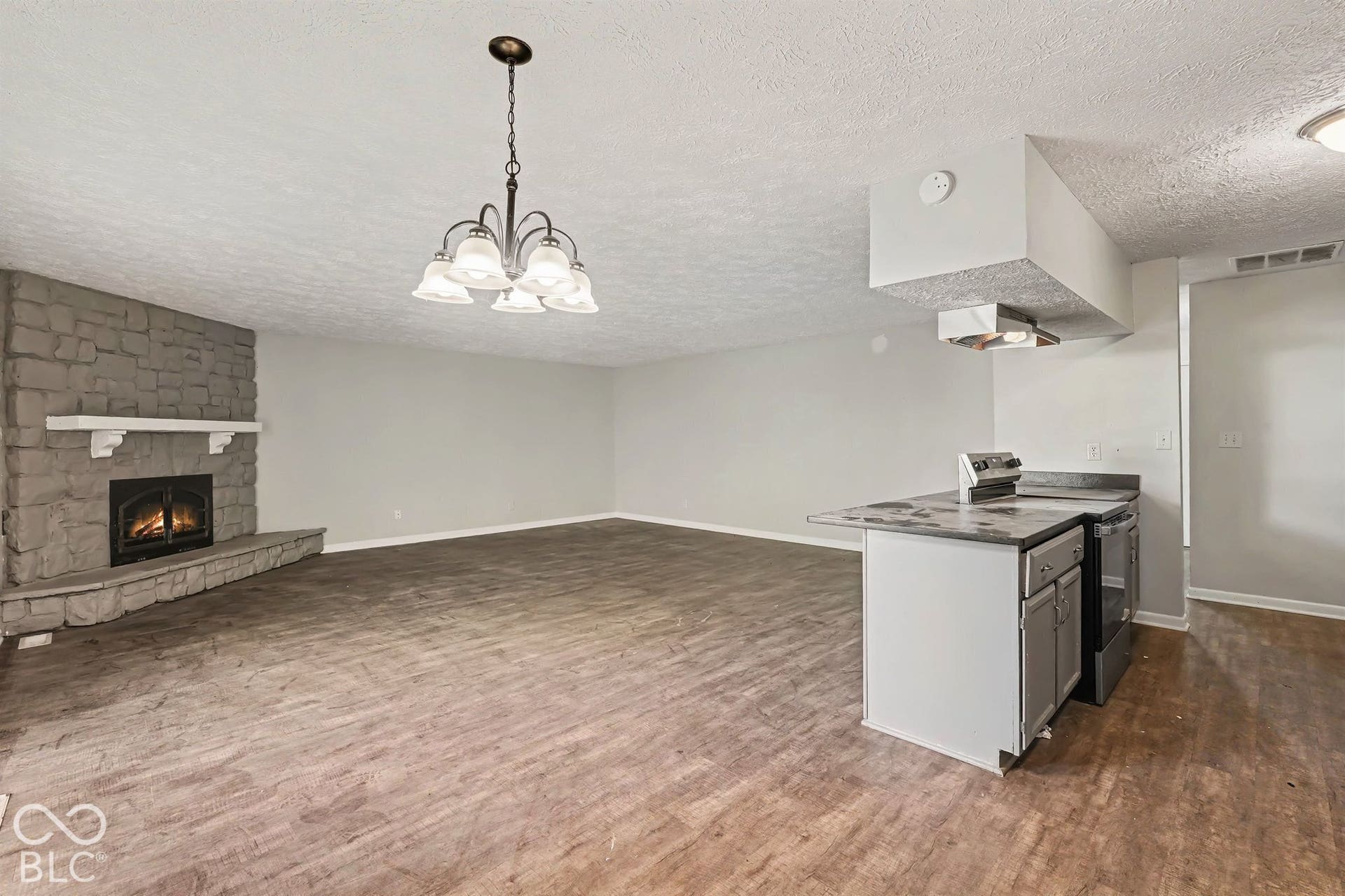 Stone fireplace with hearth and mantel, wood-finish flooring, and kitchen peninsula featuring integrated cabinetry and countertop