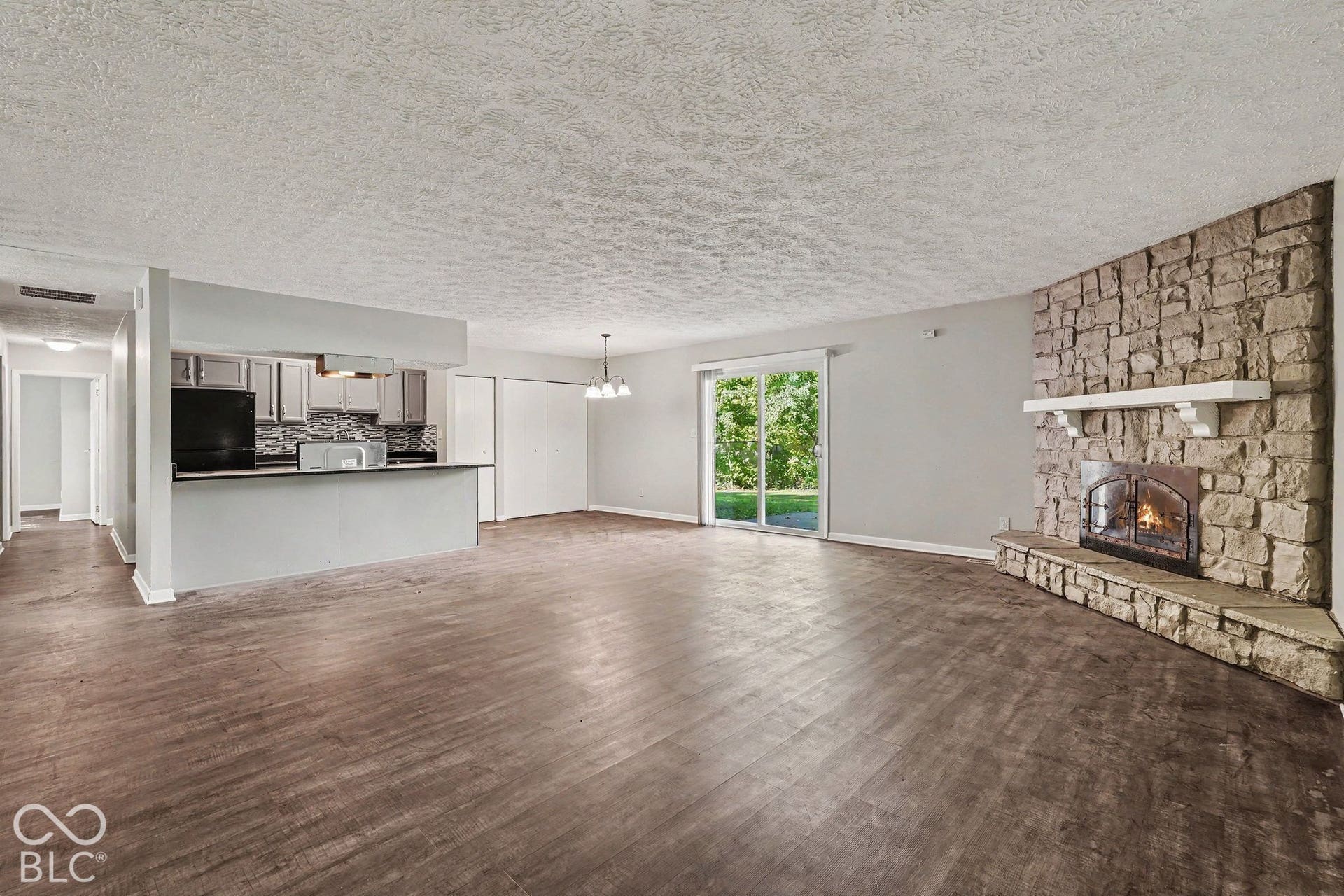 Living area featuring wood-finish flooring, a floor-to-ceiling stone fireplace with a stone hearth and mantel, breakfast bar, and sliding glass doors