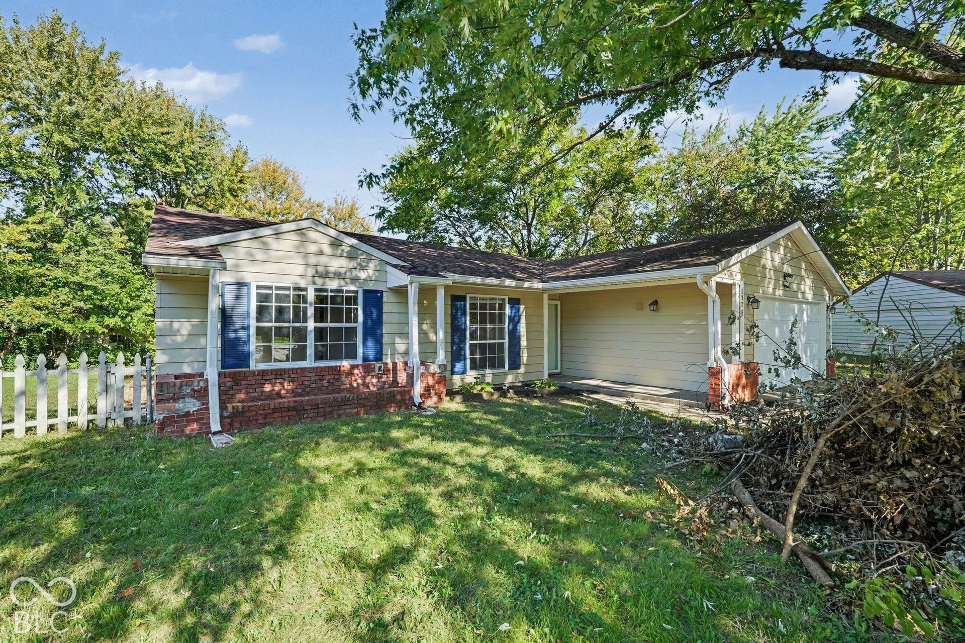 Ranch-style exterior featuring horizontal siding, brick masonry detailing, multi-pane windows with decorative shutters, a covered entryway, and a white picket fence