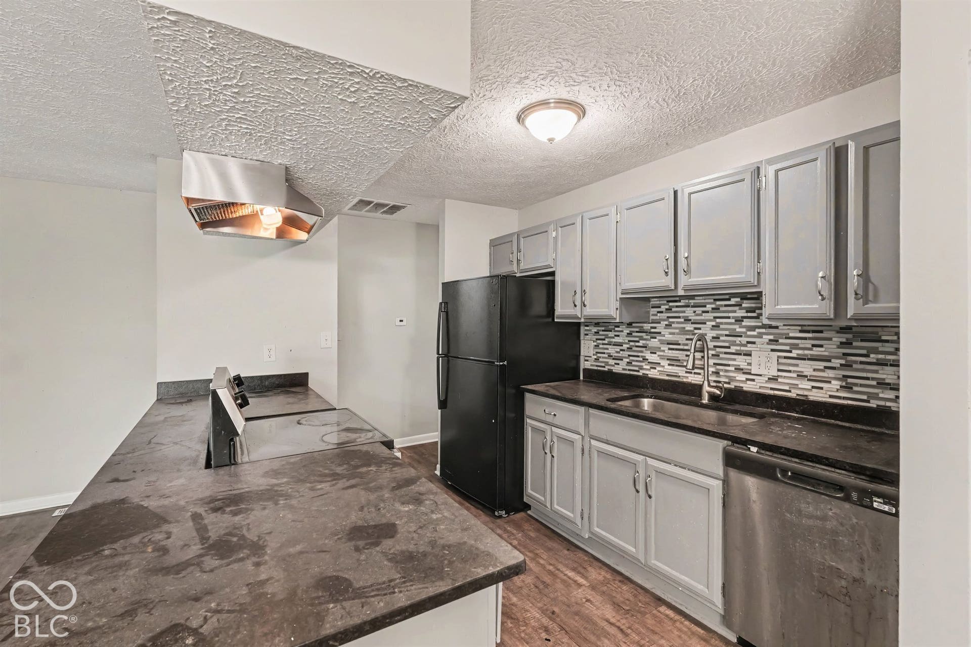 Kitchen featuring gray cabinetry, decorative mosaic tile backsplash, solid-surface countertops, built-in cooktop with stainless steel vent hood, and wood-finish flooring