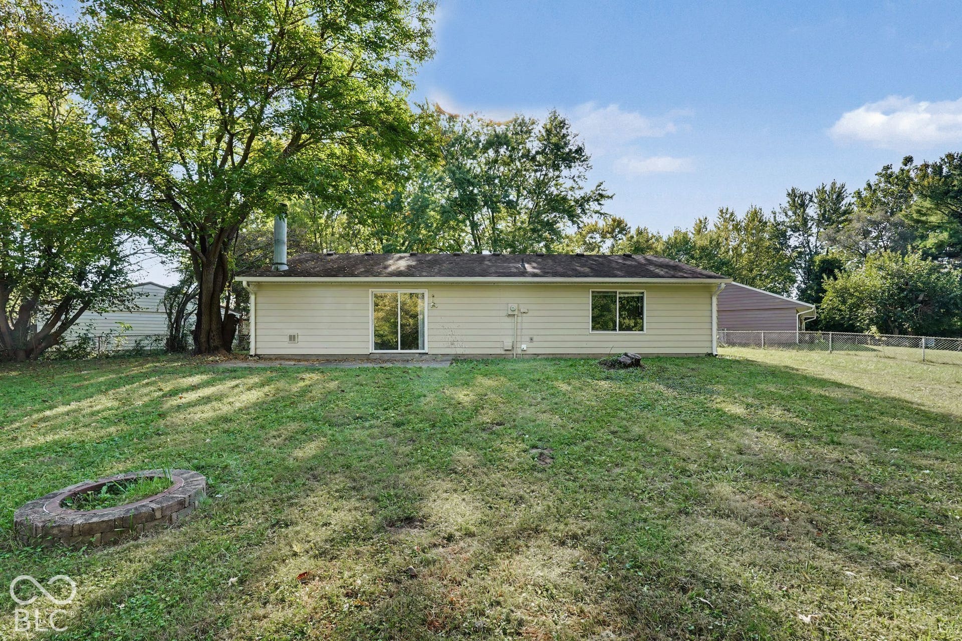 Rear exterior featuring horizontal lap siding, sliding glass doors, a brick fire pit, and mature shade trees on a expansive grass lawn