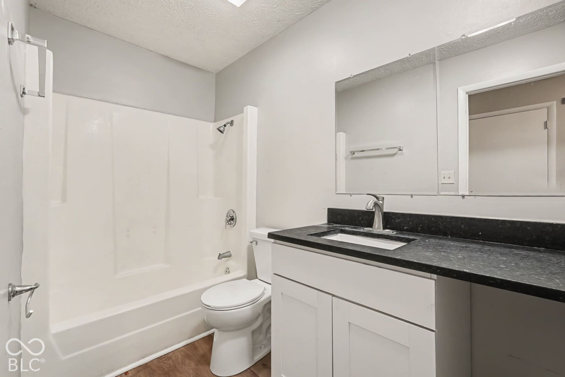 Bathroom featuring a white vanity with a dark stone countertop, integrated rectangular sink, full-width wall mirror, and a tub-shower combination with a surround