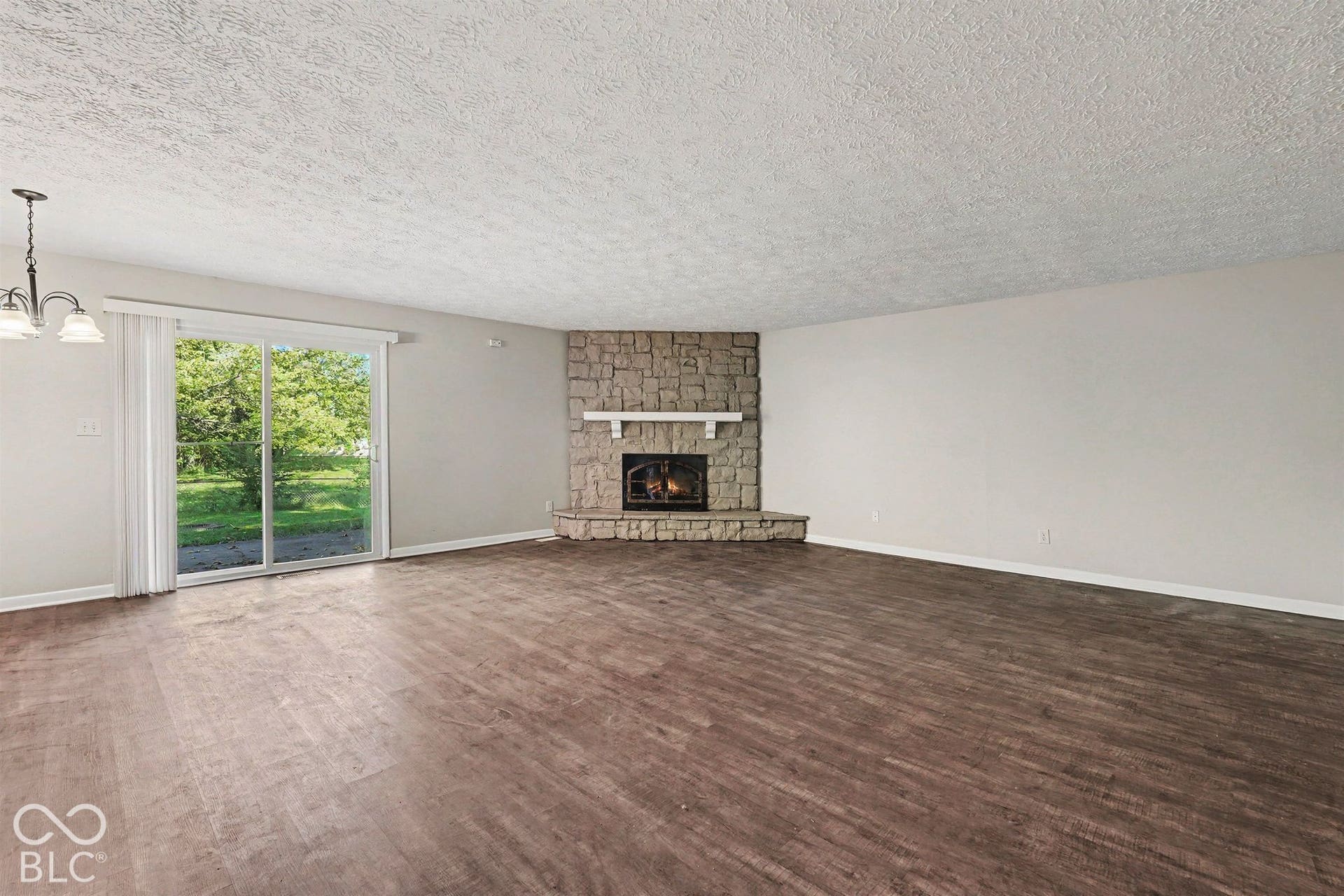 Corner stone fireplace featuring a raised hearth and mantel, wood-finish flooring, and sliding glass doors
