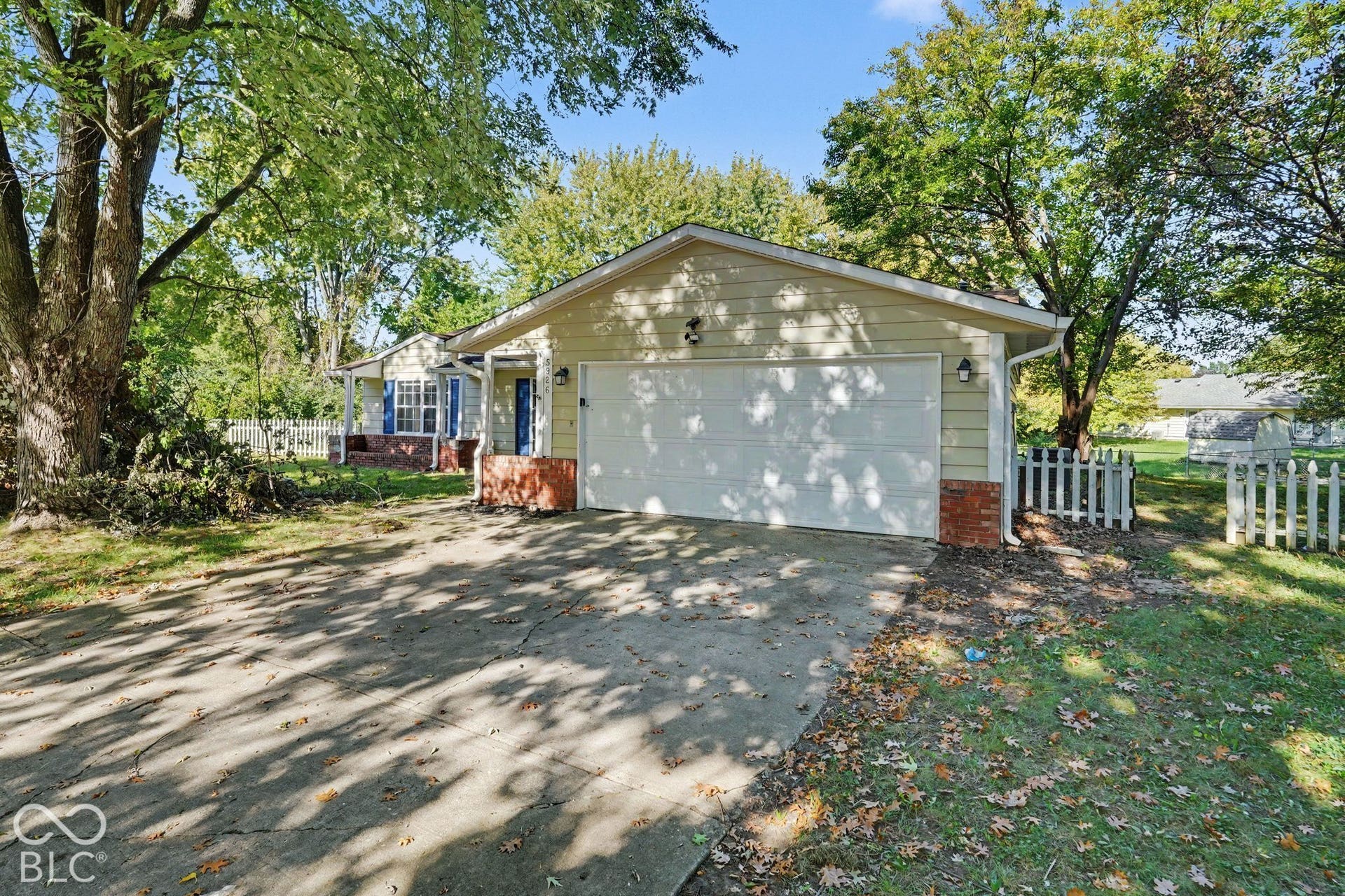 Single-story residence featuring horizontal lap siding, attached two-car garage, brick veneer accents, and perimeter picket fencing on a landscaped lot