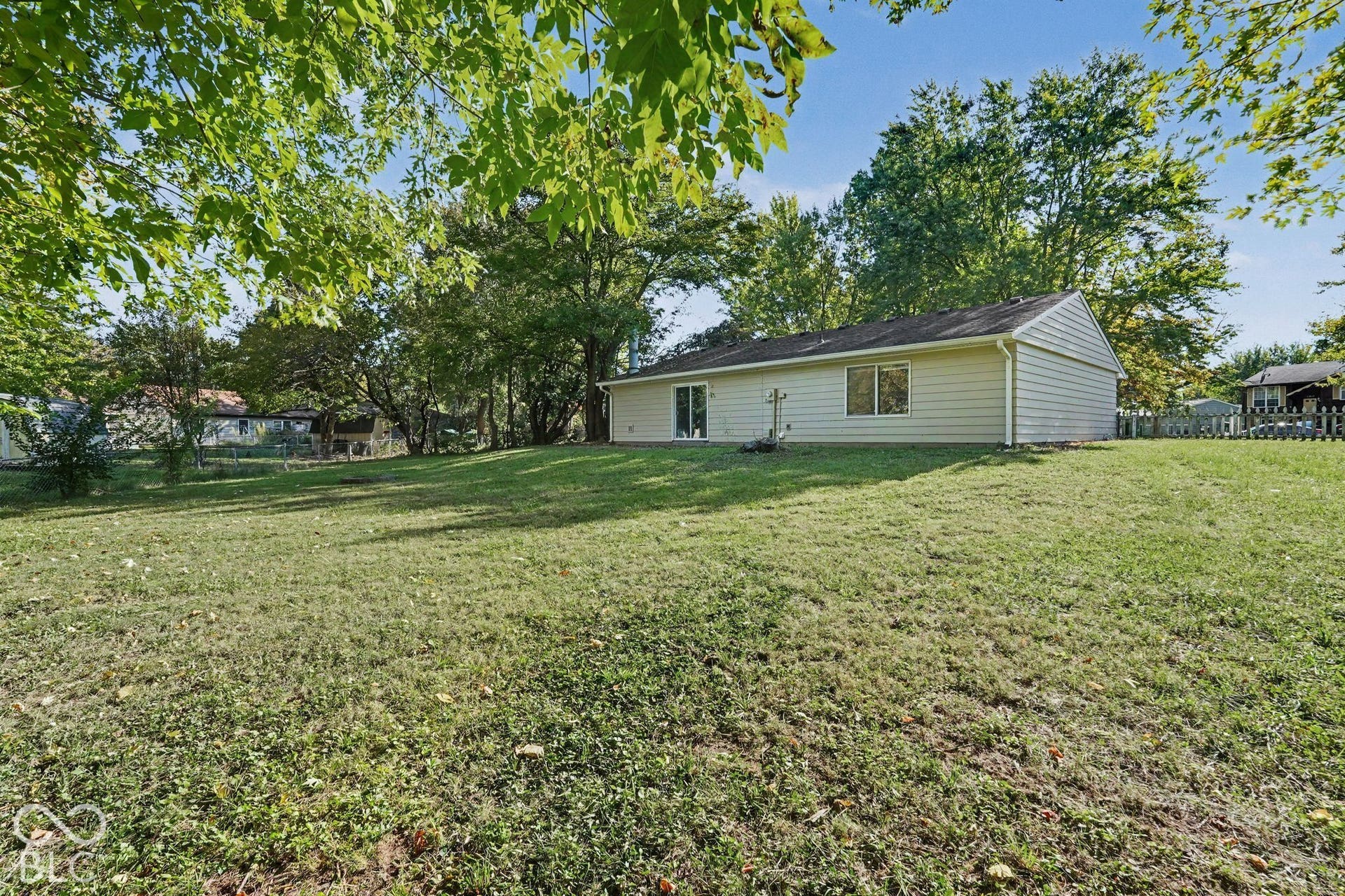 Expansive rear lawn featuring mature trees and a vinyl-sided exterior with sliding glass doors
