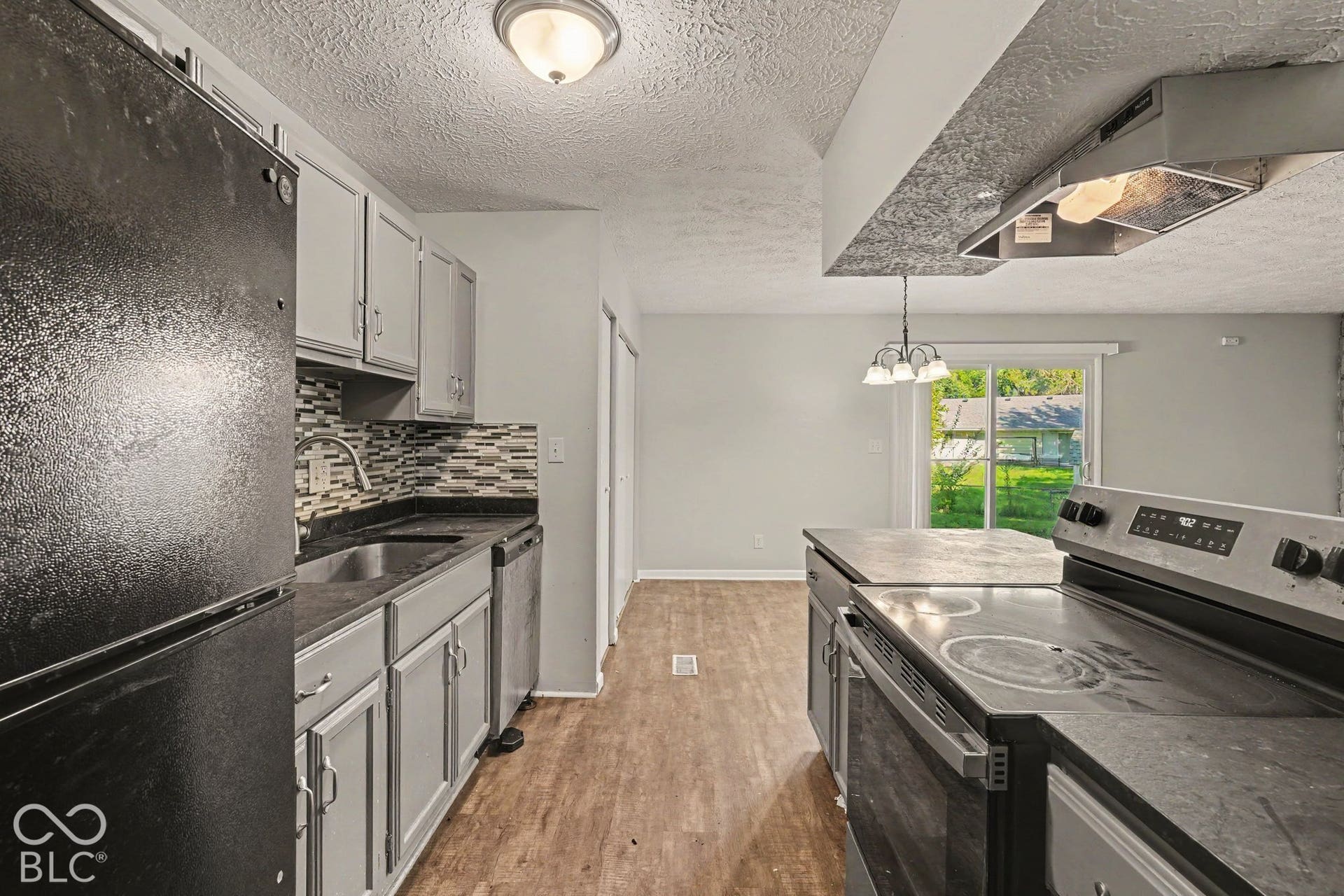 Kitchen featuring light gray cabinetry, dark countertops, a multi-tonal tile backsplash, wood-finish flooring, and a sliding glass door