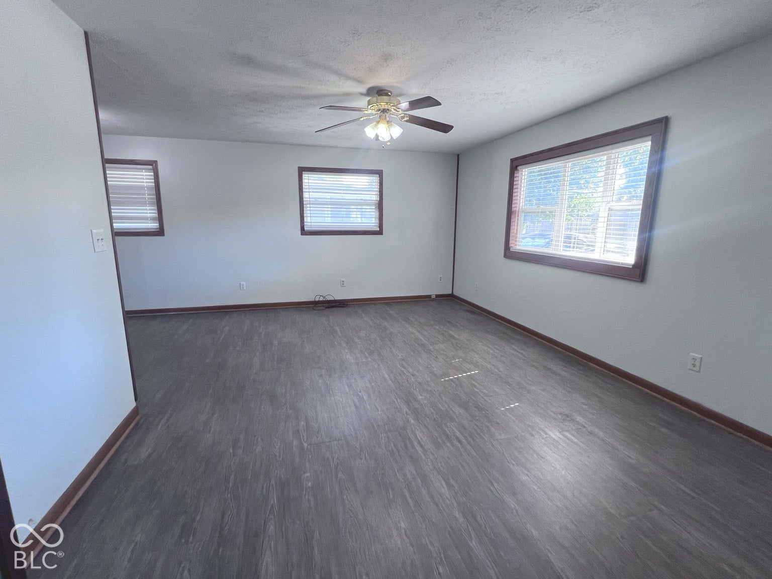 4906 W Troy Avenue, Indianapolis, IN 46241 Interior room featuring wood-finish flooring, neutral wall tones, triple windows with dark-finish trim, and a ceiling-mounted fan with integrated light fixture