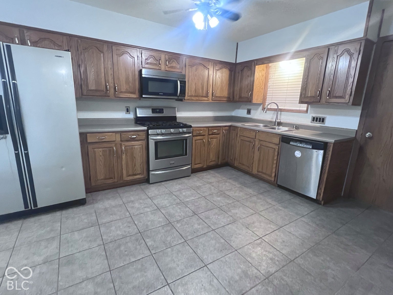 4906 W Troy Avenue, Indianapolis, IN 46241 Kitchen featuring wood cabinetry, stainless steel appliances including a gas range and microwave, neutral tile flooring, and a double-basin stainless steel sink with a high-arch faucet
