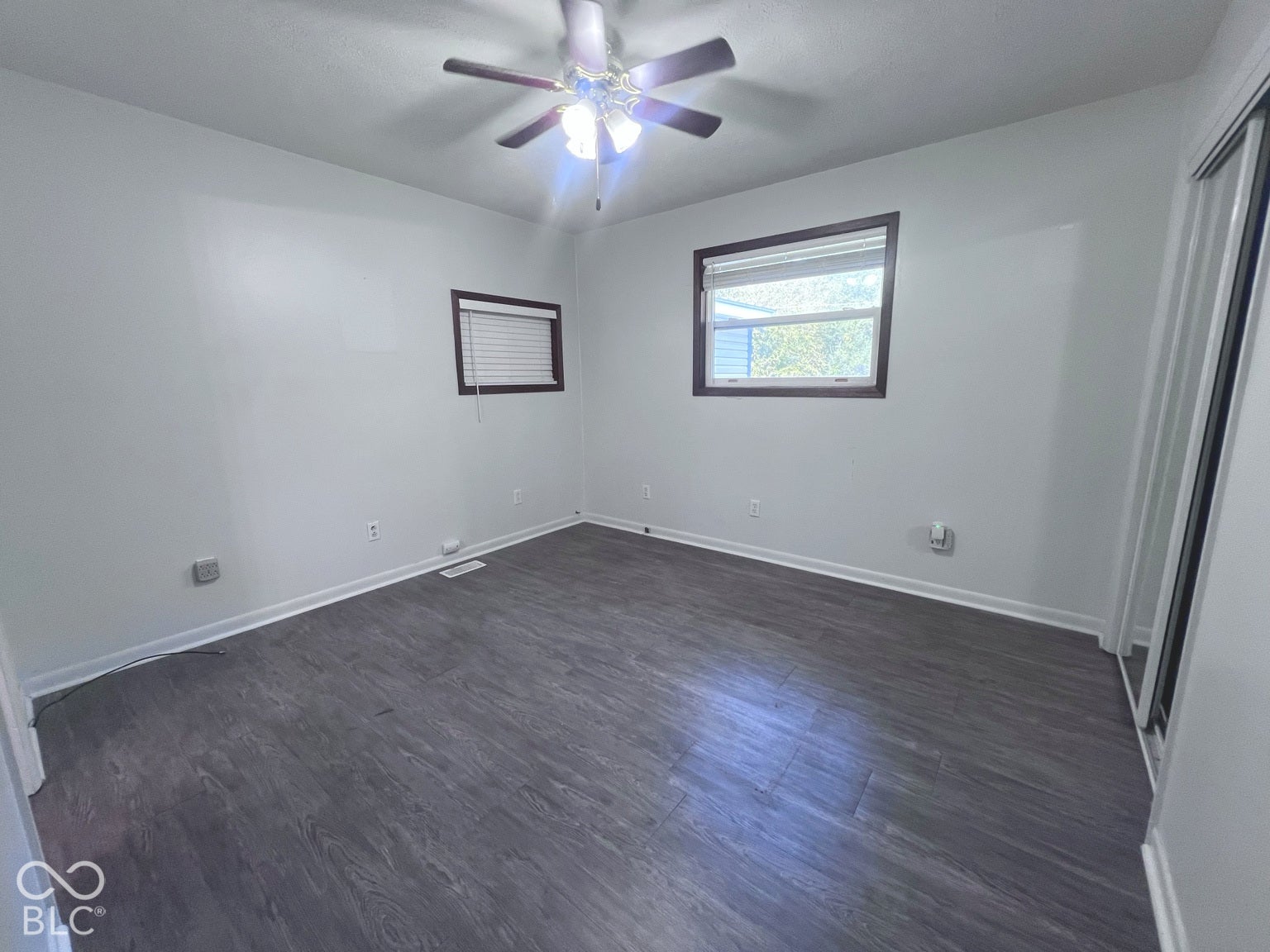 4906 W Troy Avenue, Indianapolis, IN 46241 Bright, spacious bedroom featuring dark wood-finish flooring, ceiling fan with integrated lighting, and multiple windows allowing natural light throughout the room