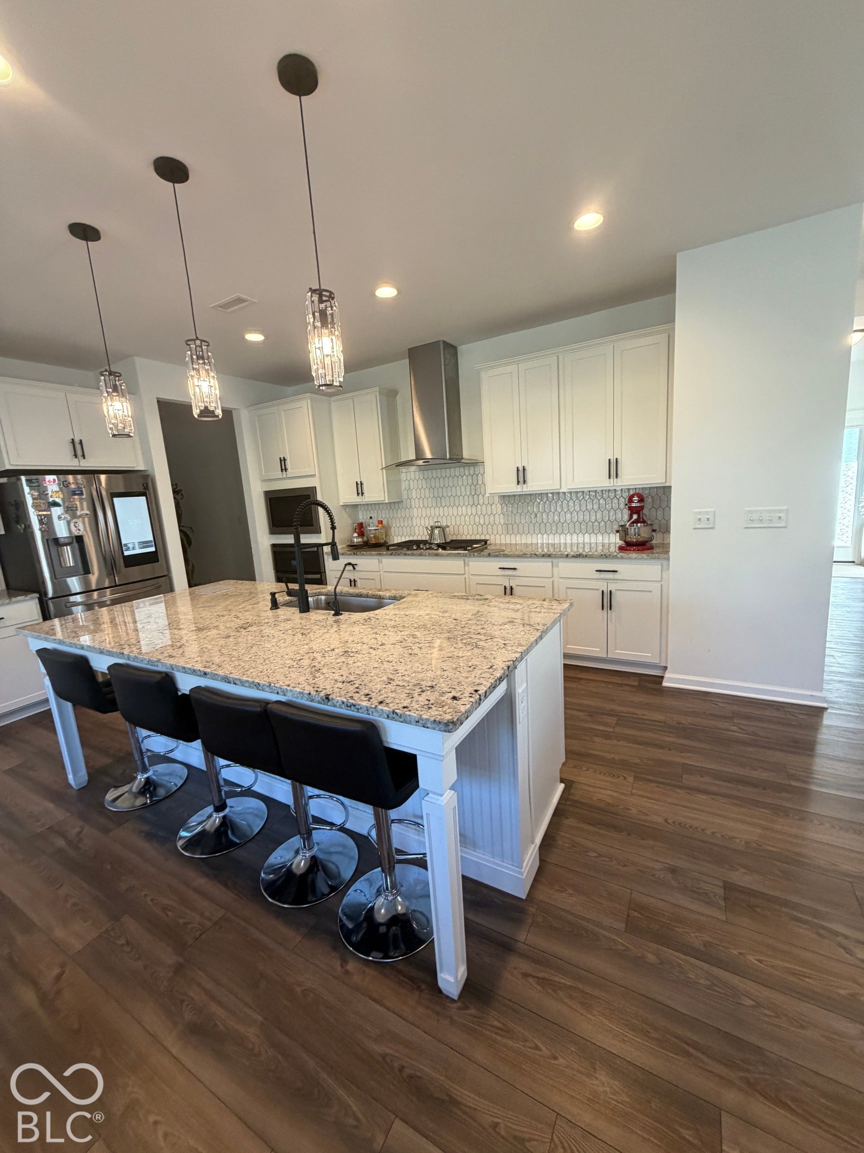 Kitchen featuring a center island with stone-finish countertops, shaker-style cabinetry, a stainless steel chimney-style range hood, patterned tile backsplash, and wood-finish flooring