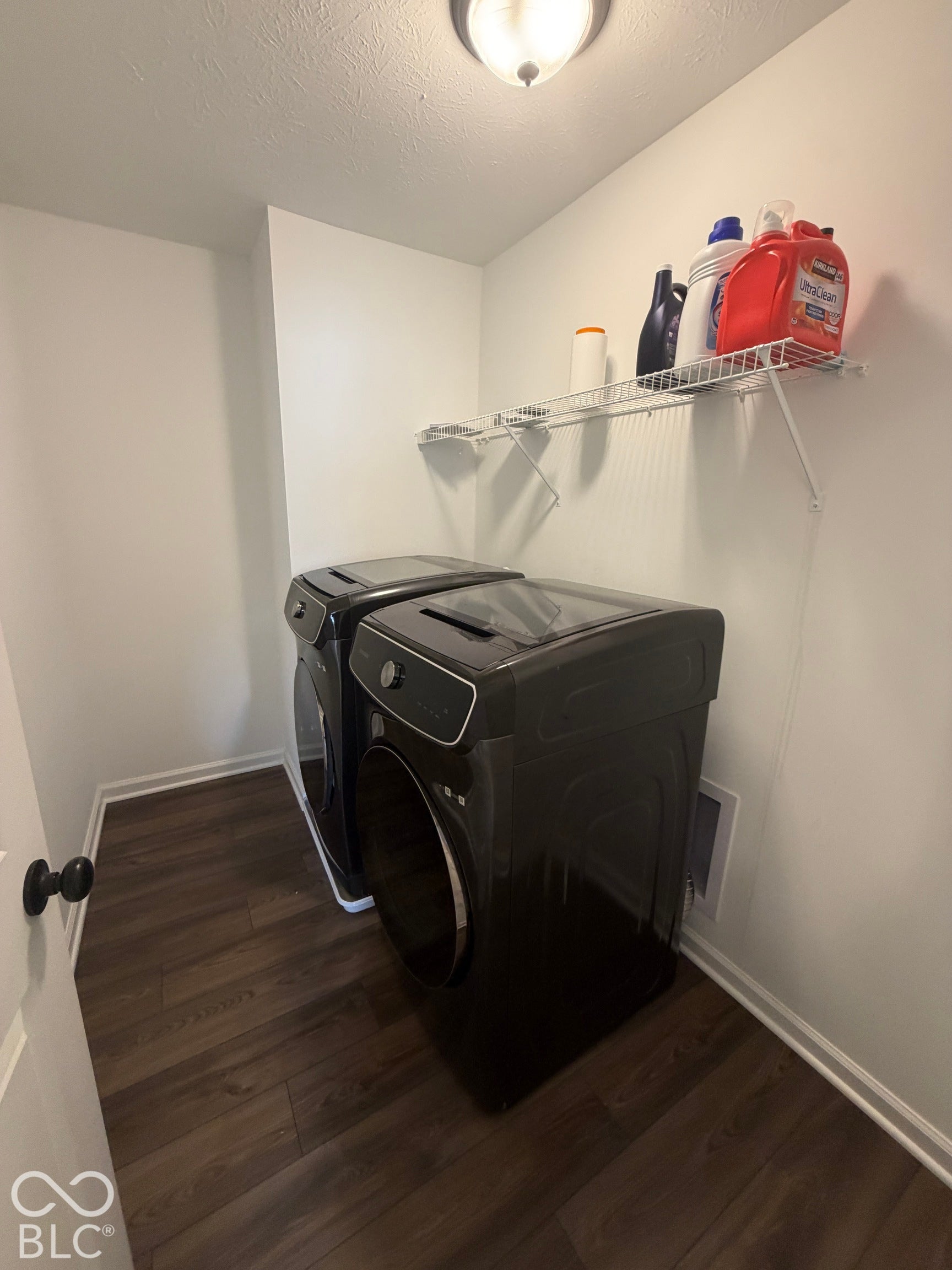 Laundry area featuring wood-finish flooring, white walls, and a wall-mounted wire shelving unit