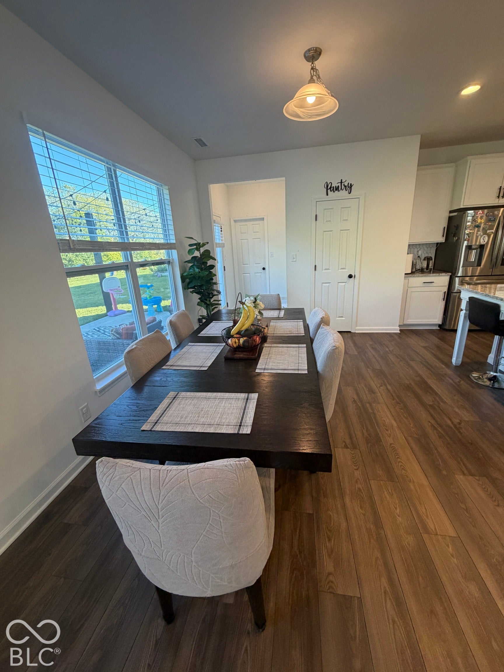 Wood-finish flooring throughout, large multi-pane window with integrated blinds, pendant lighting, and dedicated pantry closet