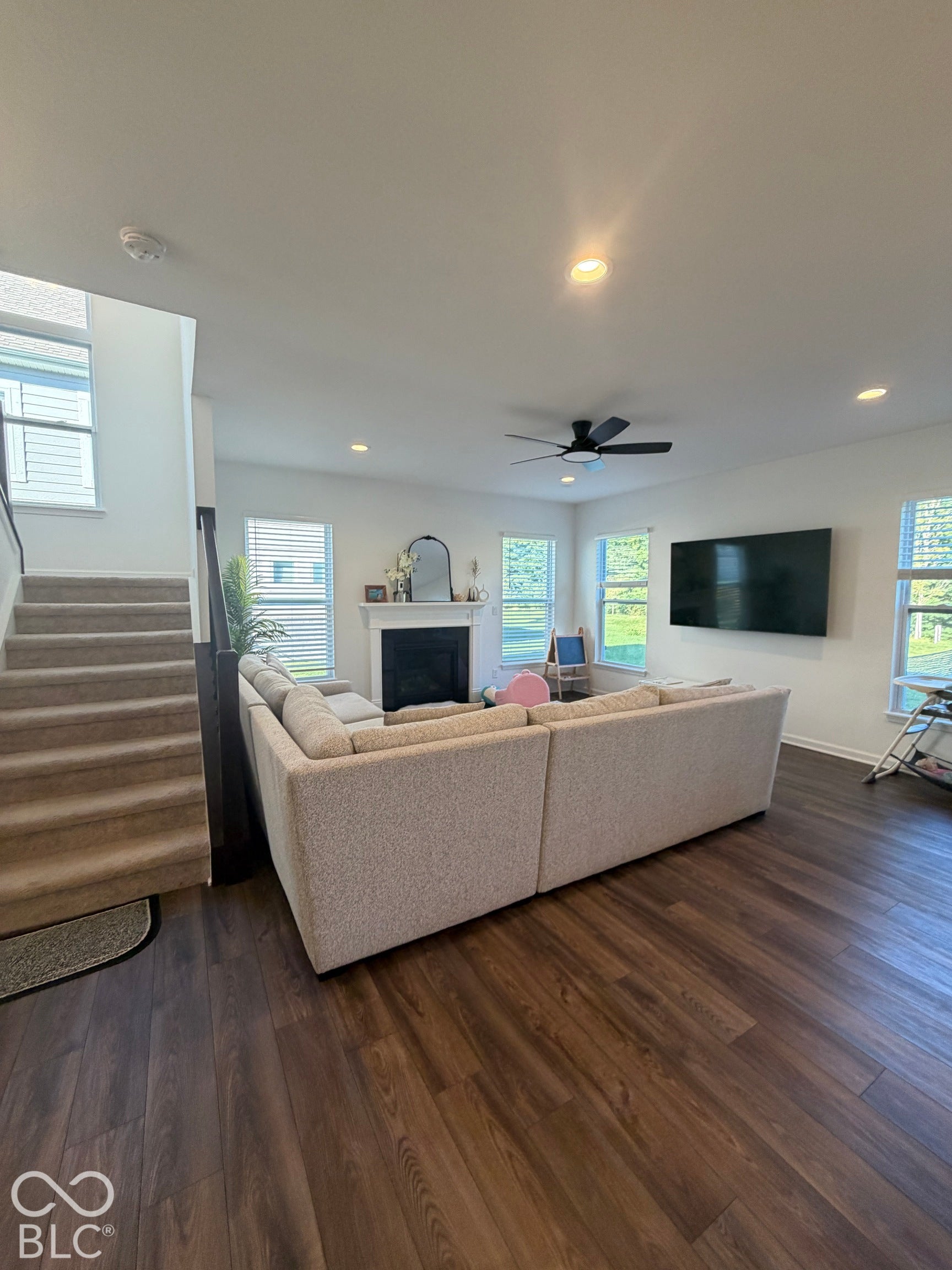 Living area featuring wood-finish flooring, fireplace with a decorative mantel, recessed lighting, ceiling fan, and large windows