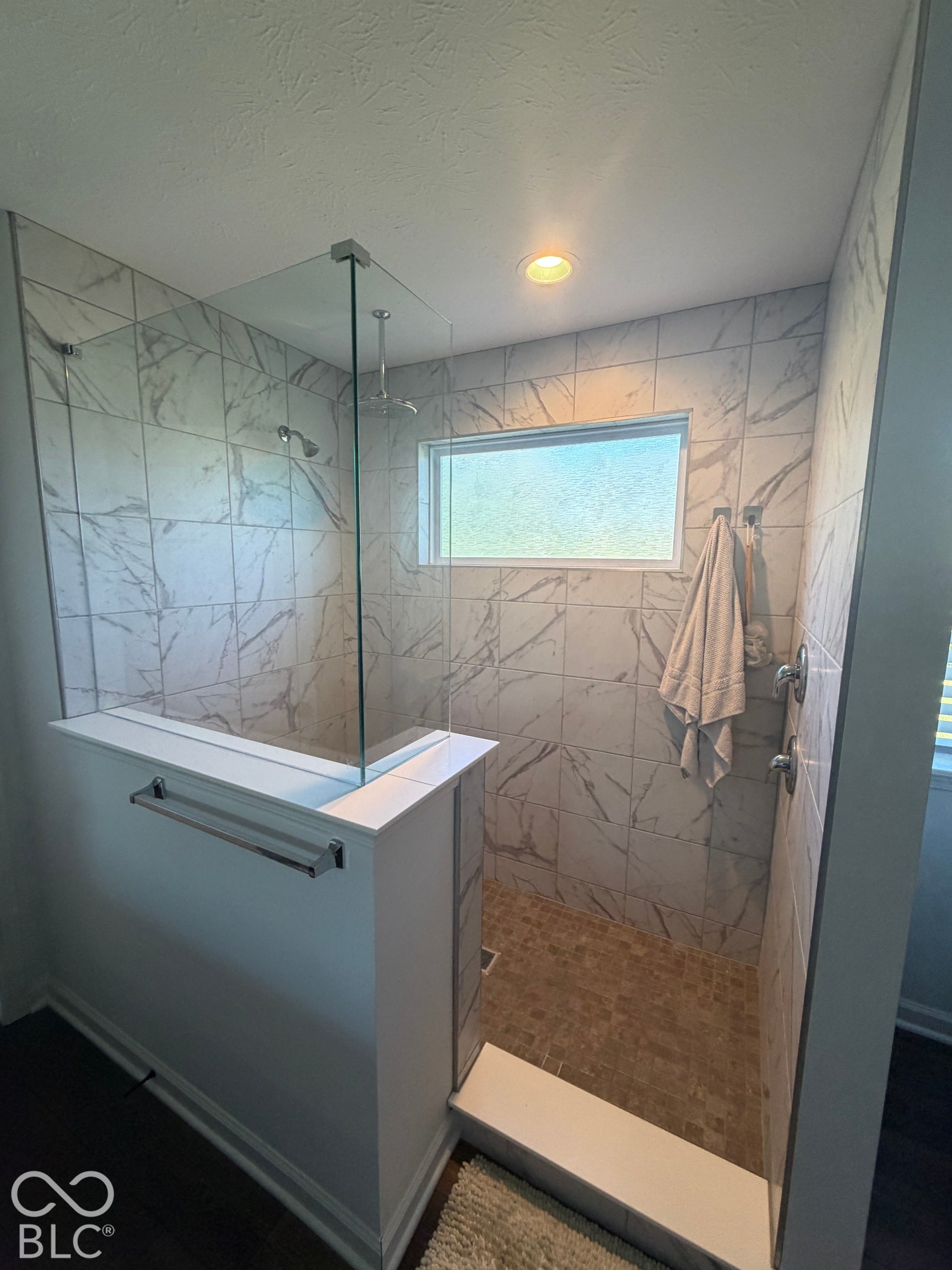 Walk-in shower featuring floor-to-ceiling stone-pattern tile, a frameless glass enclosure, a ceiling-mounted rainfall showerhead, and a mosaic tile floor