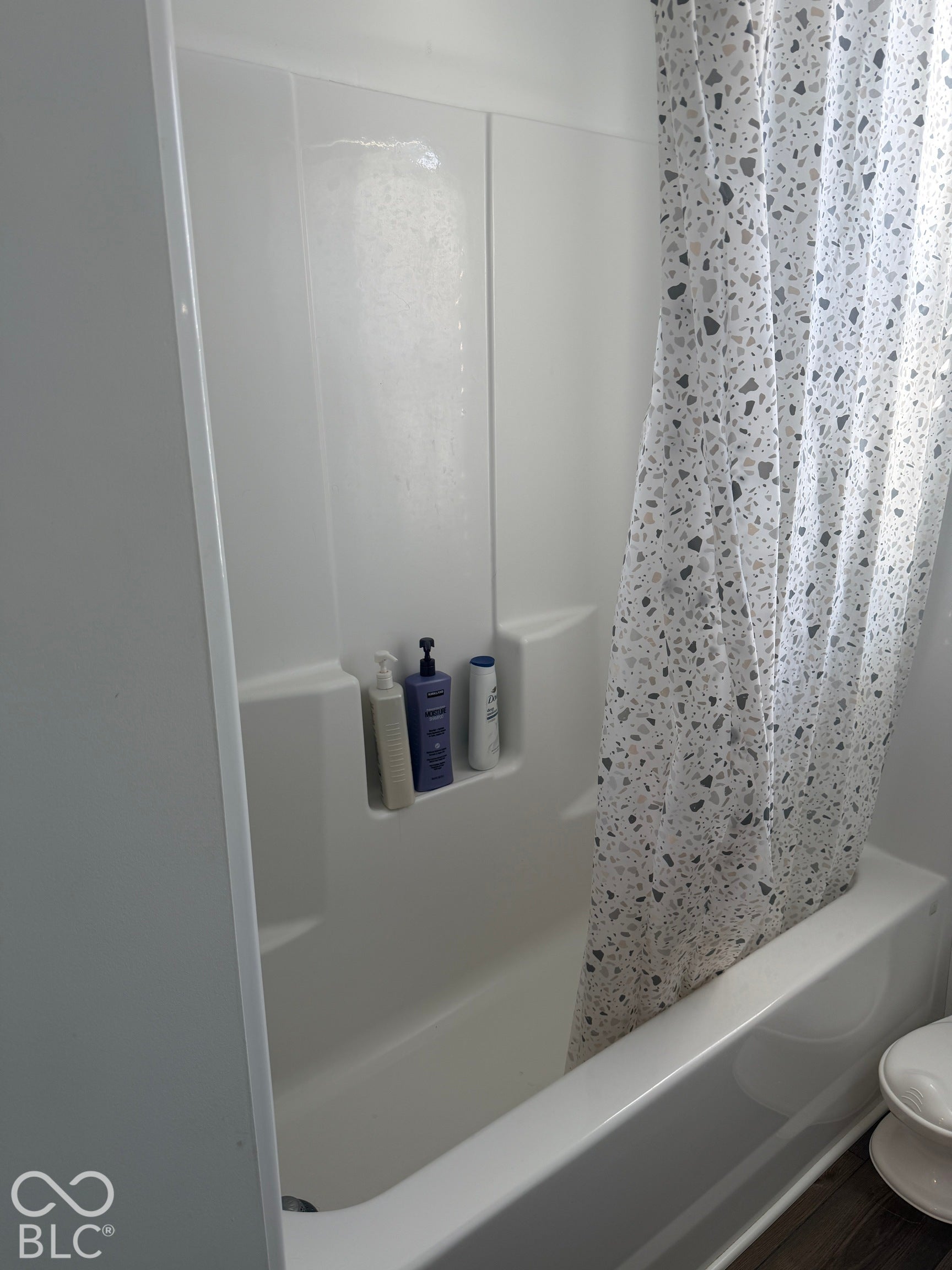 Bathtub and shower combination featuring a seamless white surround with a built-in recessed storage niche
