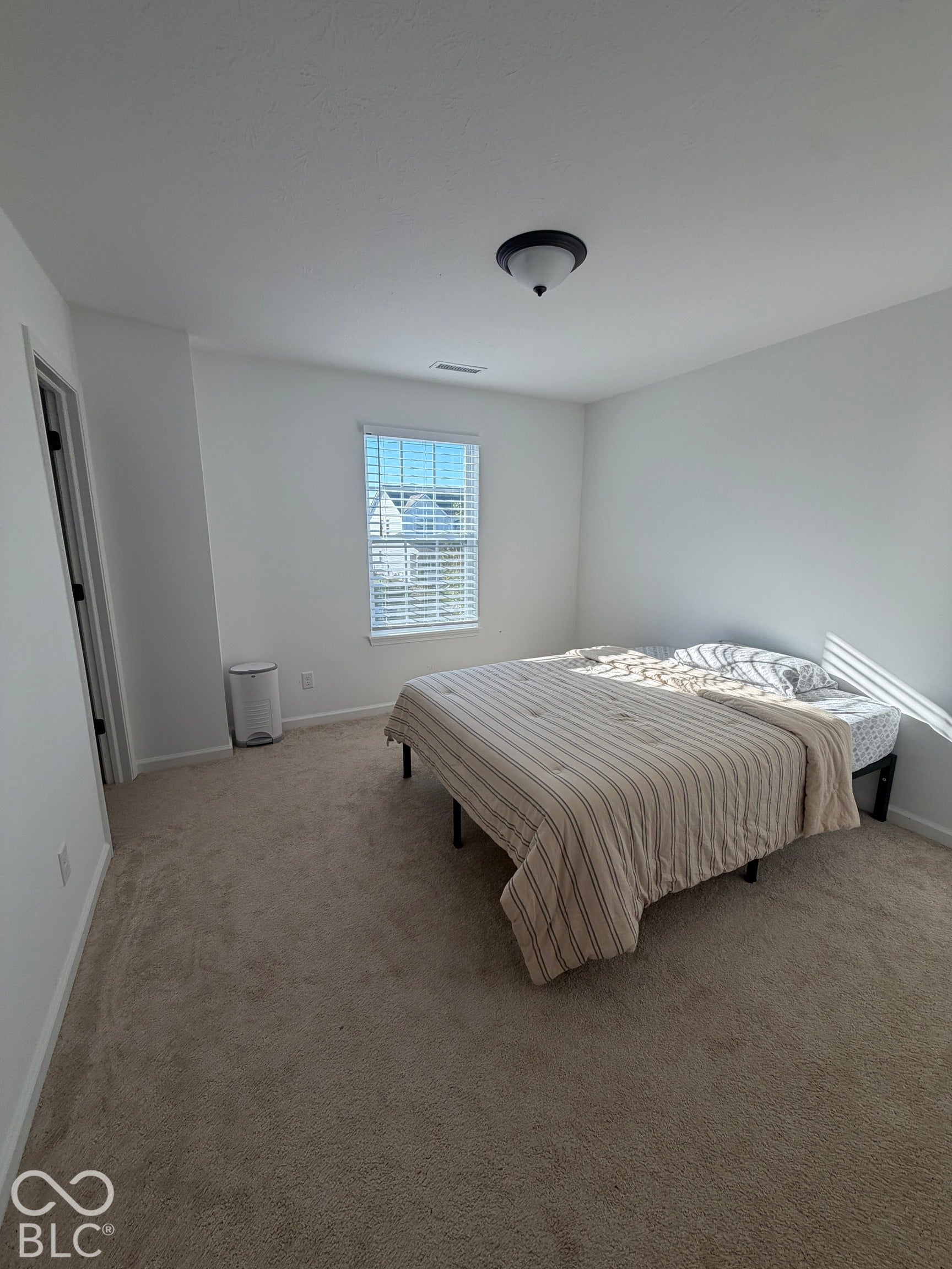 Neutral-toned carpeting, crisp wall finishes, window with horizontal blinds, and a semi-flush mount ceiling fixture