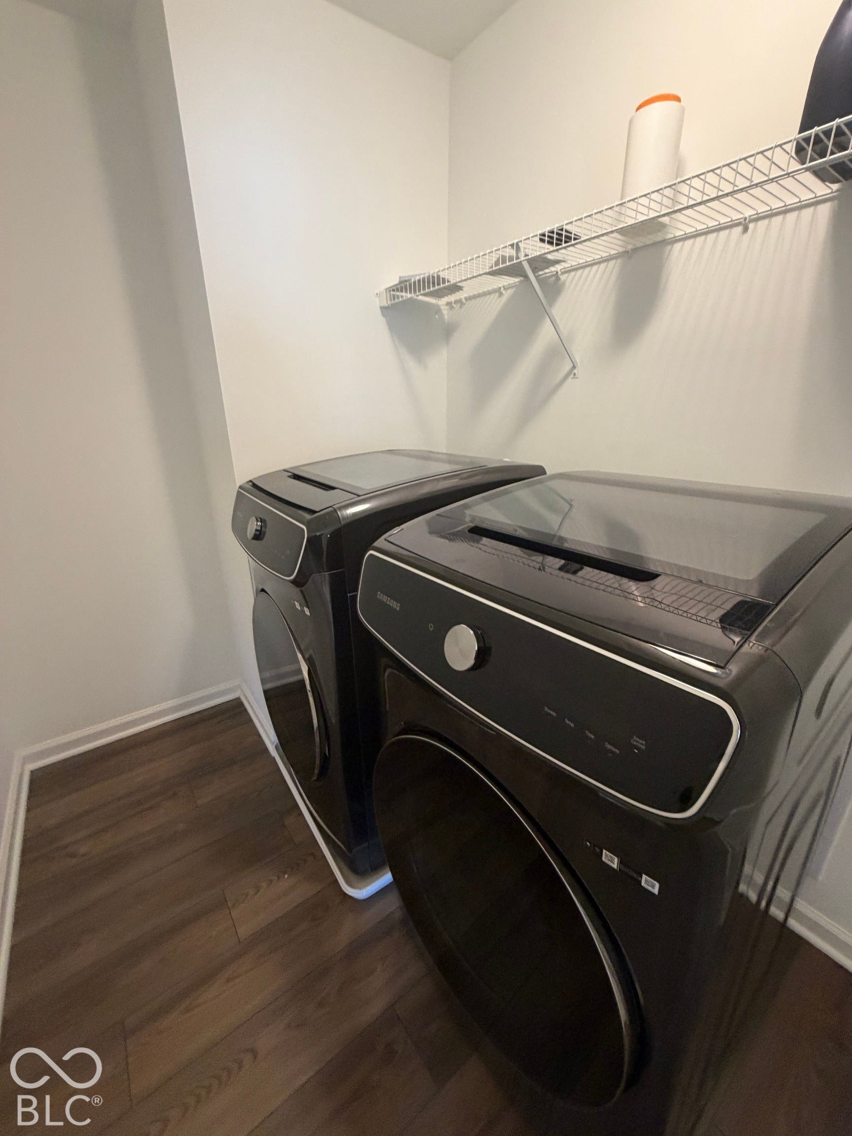 Laundry area featuring dark-toned washing machine and dryer, wood-finish flooring, and wall-mounted wire shelving
