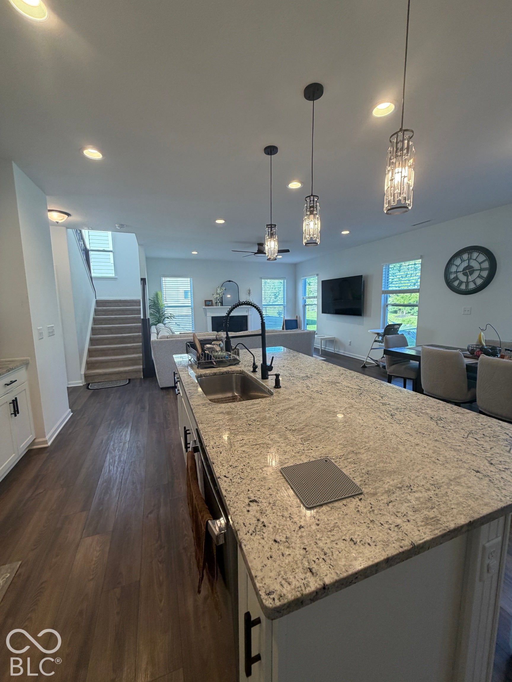 Kitchen island with stone countertop, undermount stainless steel sink, matte black faucet, pendant lighting, and wood-finish flooring