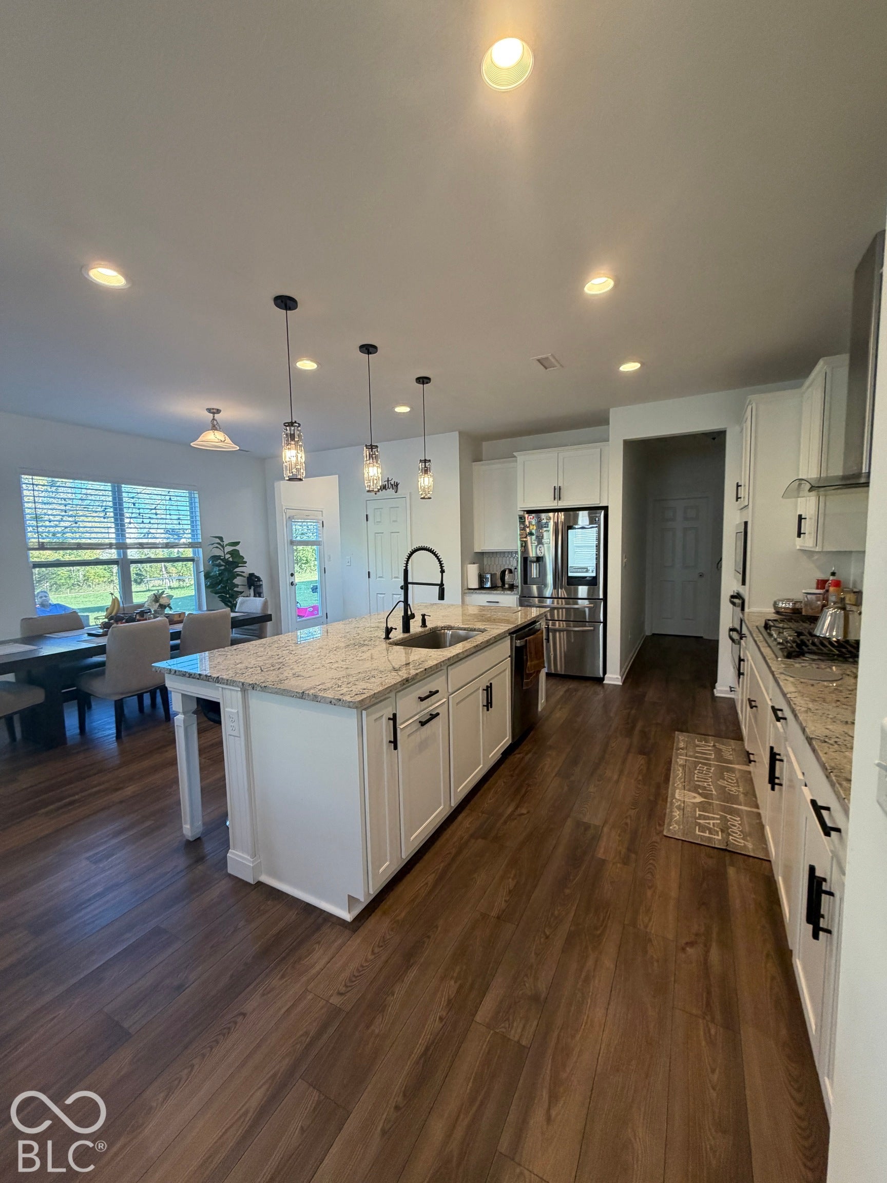 Kitchen featuring a central island with stone countertops, white shaker-style cabinetry, stainless steel appliances, pendant lighting, and wood-finish flooring