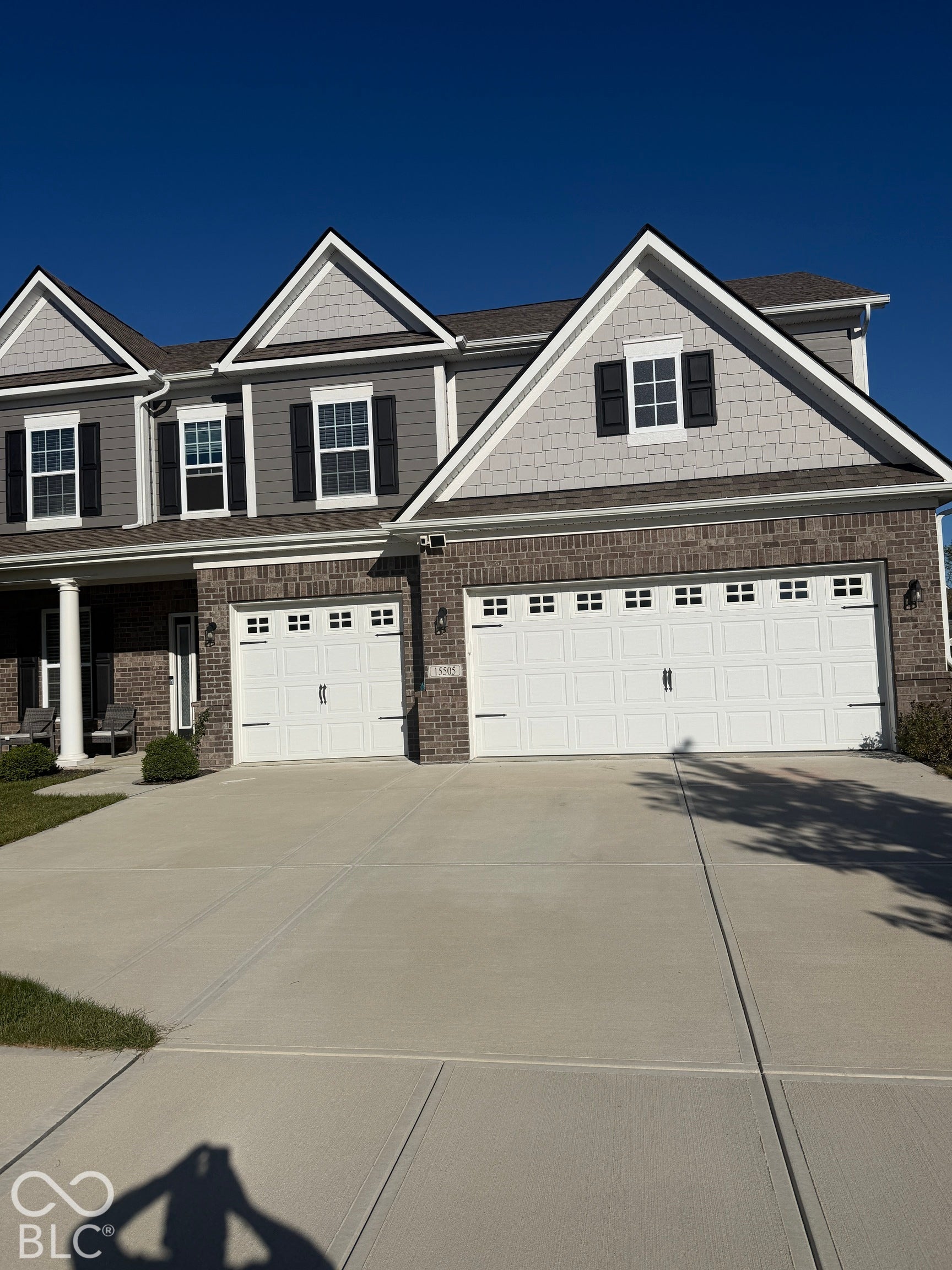 Multi-level exterior featuring a brick and composite shingle facade, decorative gable accents, carriage-style garage doors with window inserts, and black paneled shutters