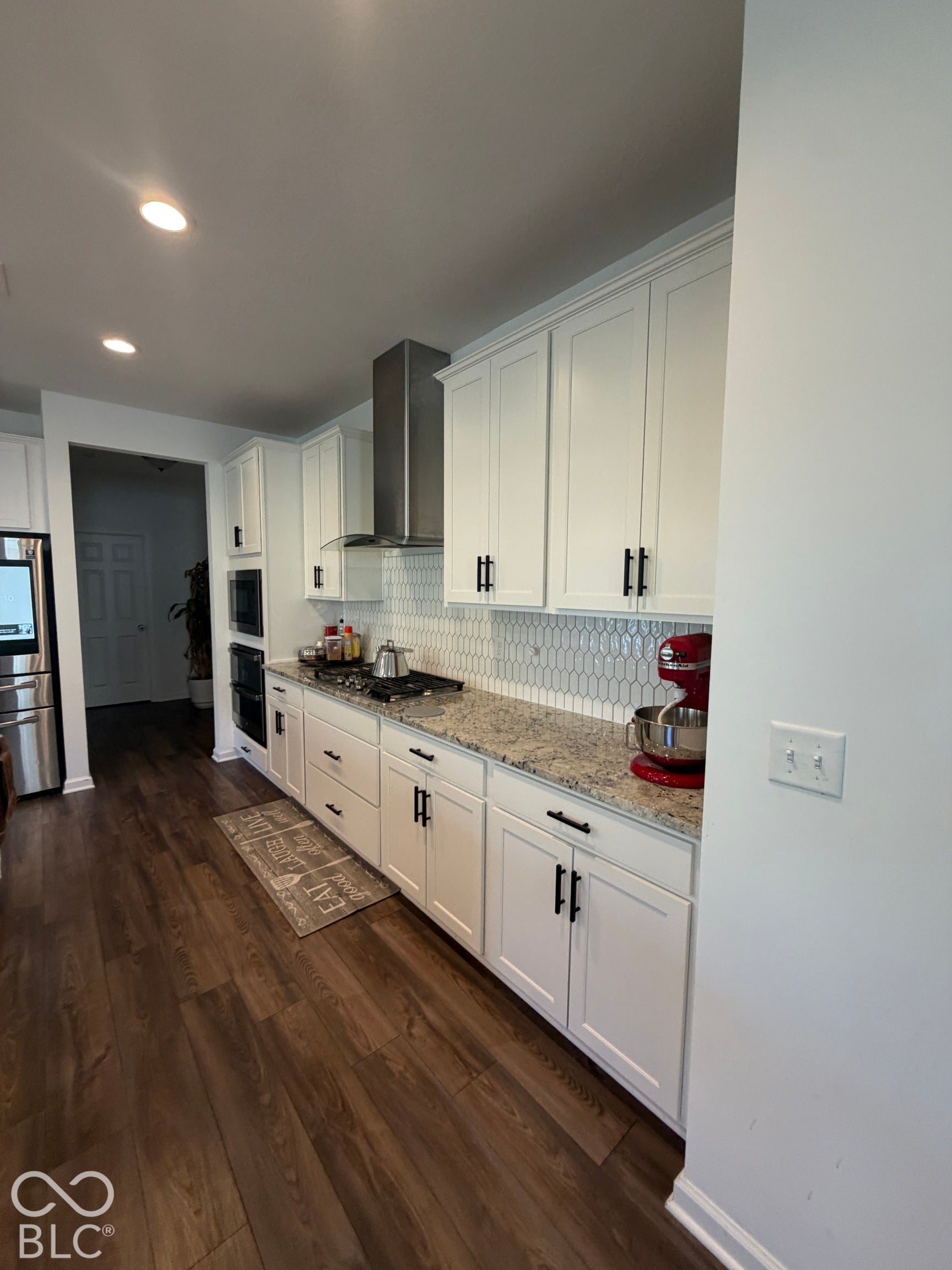 Kitchen featuring white cabinetry, stone countertops, picket-tile backsplash, stainless steel chimney-style range hood, and wood-finish flooring