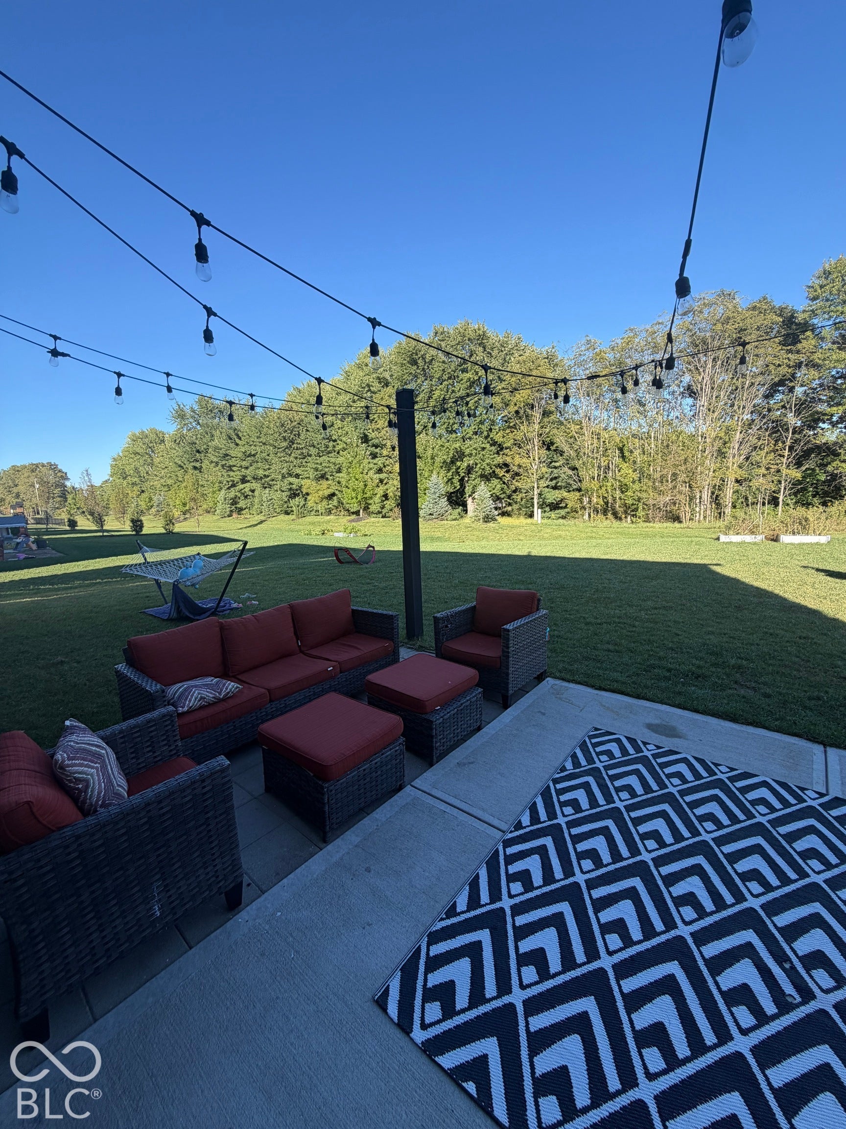Concrete patio featuring overhead string lighting and an expansive lawn
