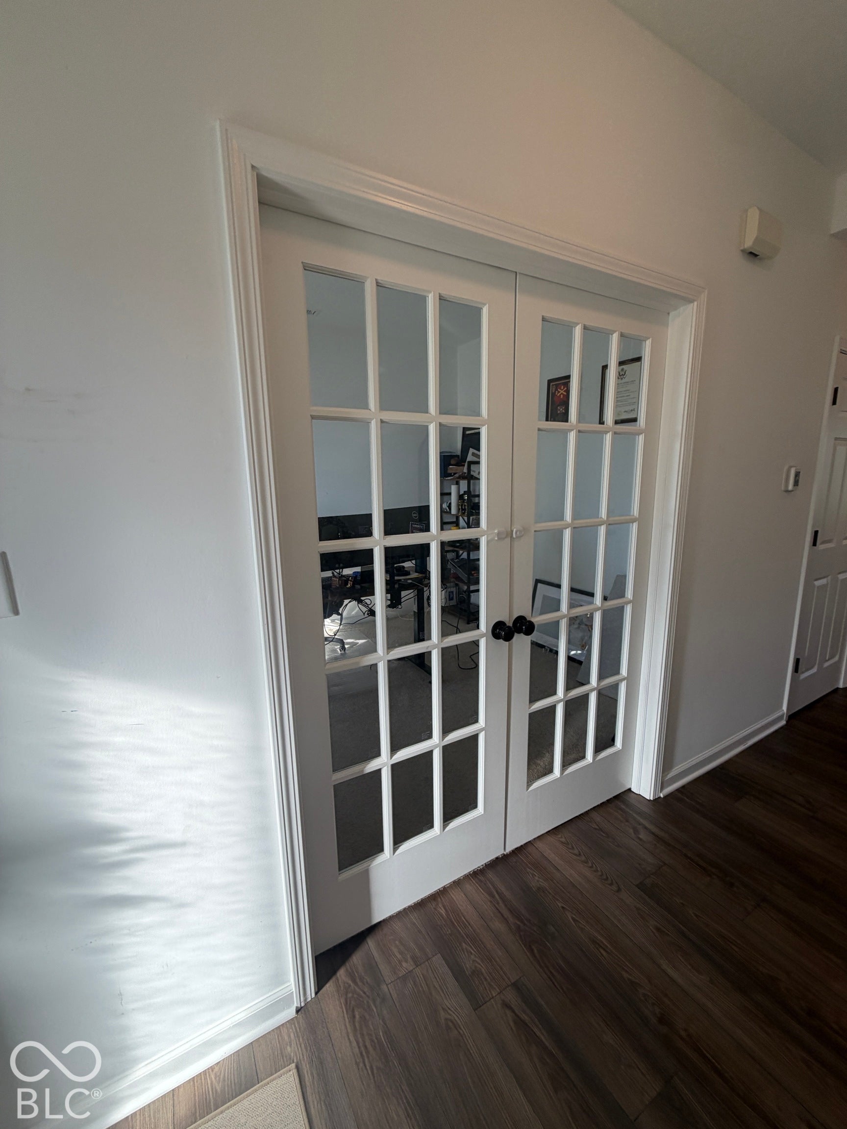 Double French doors featuring glass panes, white frames, and matte black hardware over wood-finish flooring