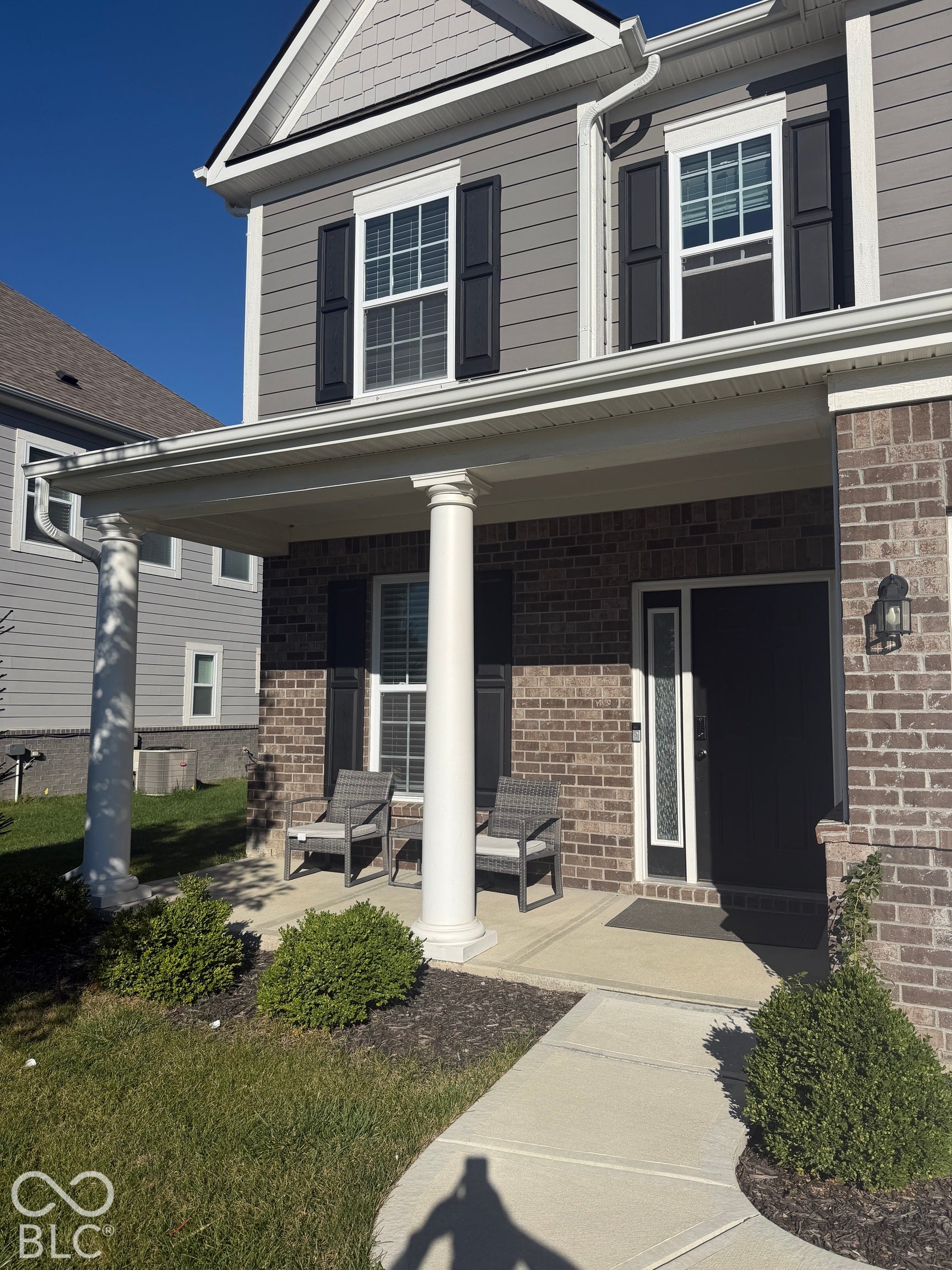 Exterior facade featuring a brick and horizontal siding finish, a covered front porch with classic columns, a concrete walkway, and decorative window shutters