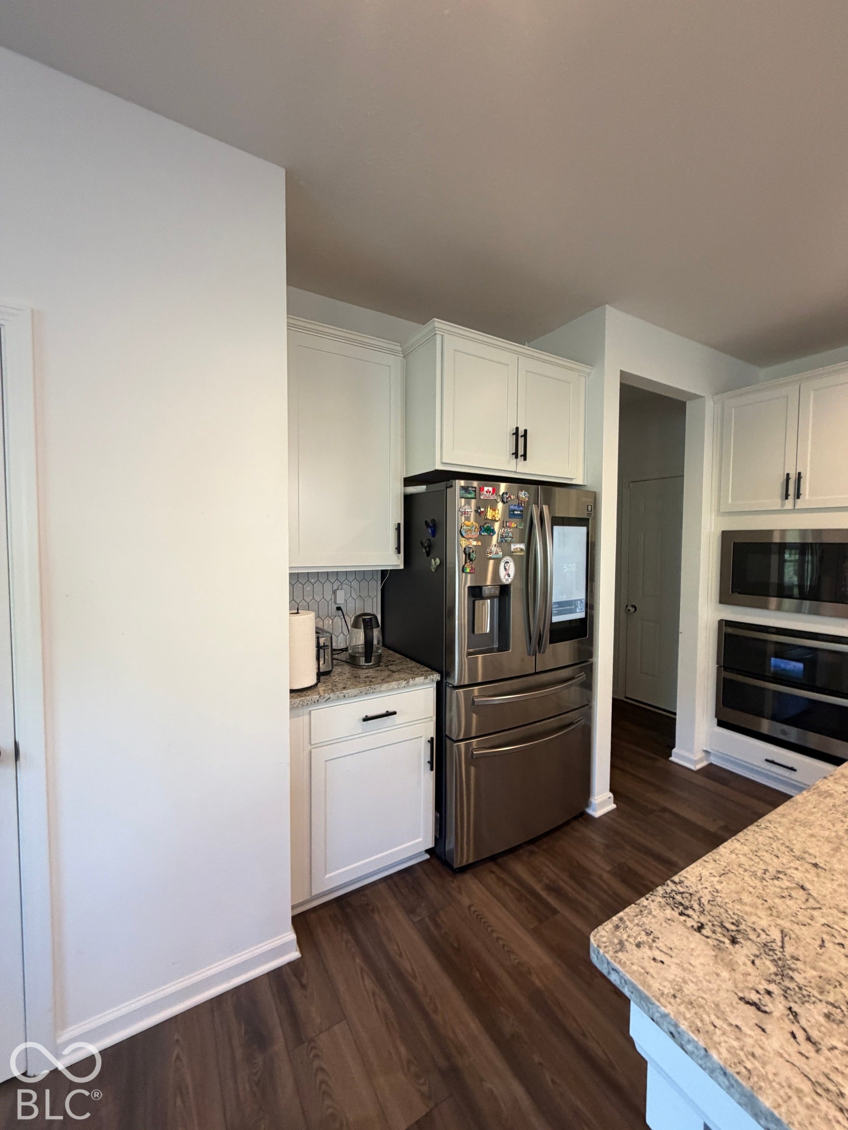 Kitchen featuring white cabinetry with matte black hardware, stone-surface countertops, wood-finish flooring, and built-in stainless steel appliances