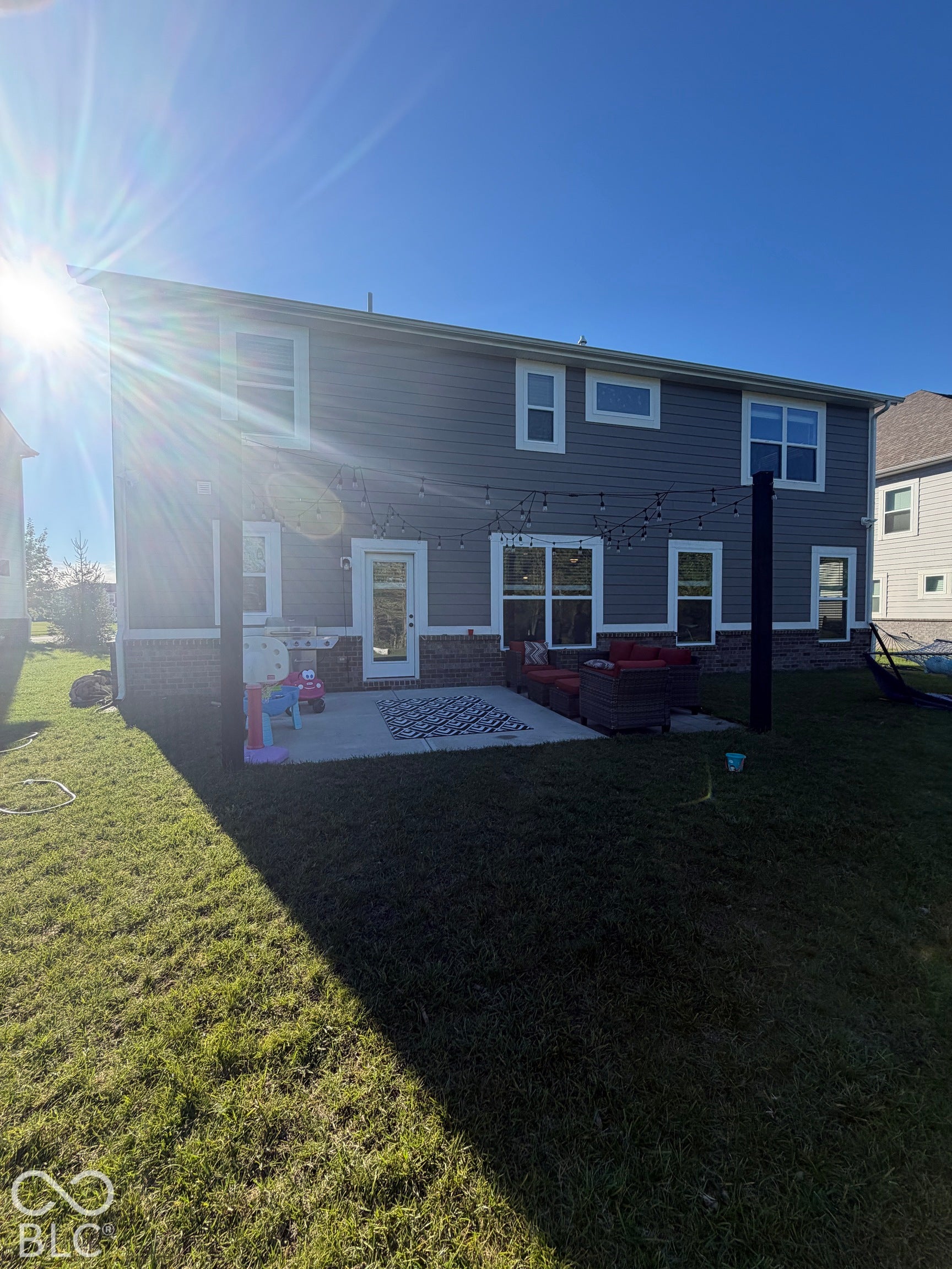 Rear exterior featuring horizontal lap siding, a brick masonry foundation, a concrete patio, and a pergola structure