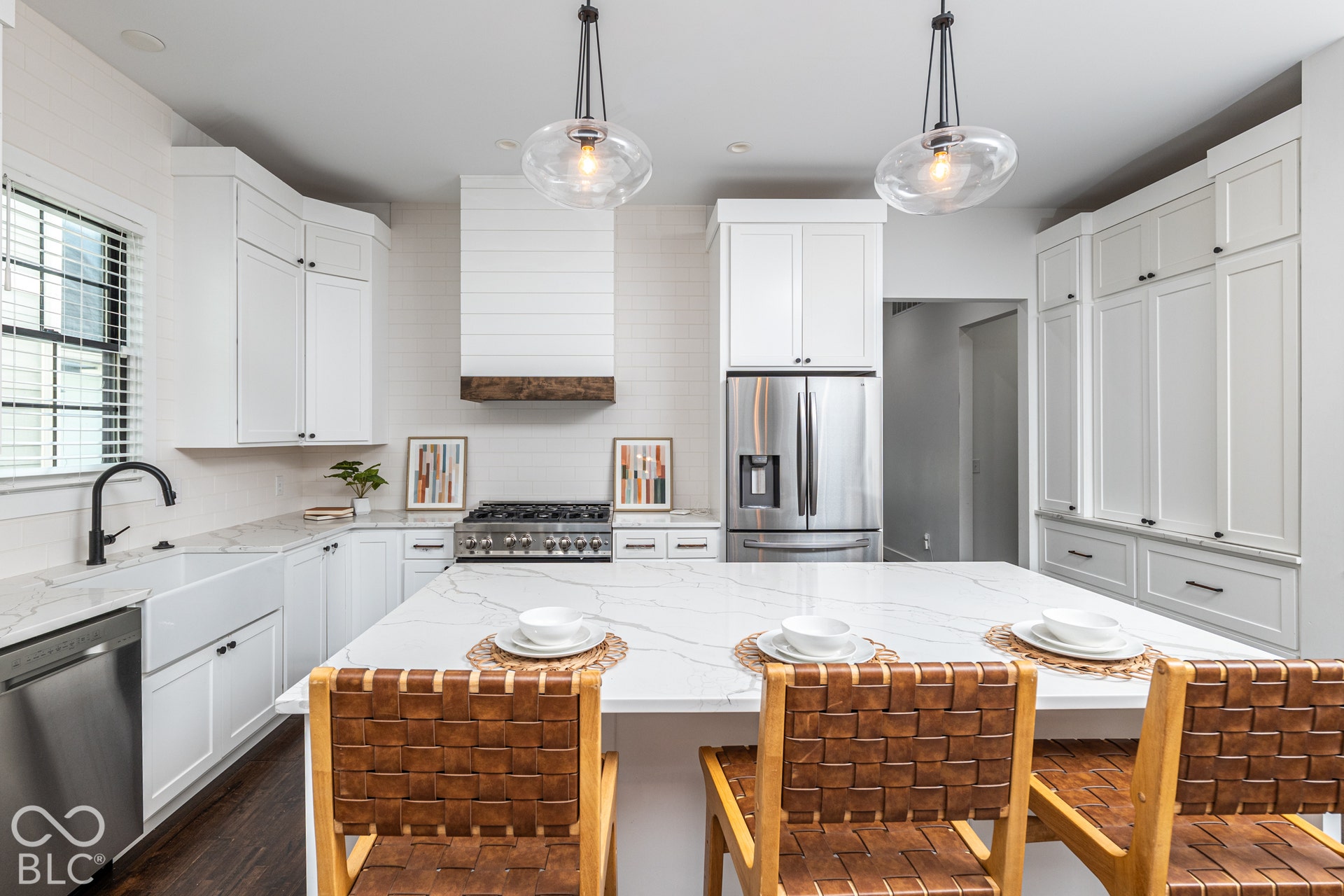 1401 Olive Street, Indianapolis, IN 46203 Kitchen featuring white shaker-style cabinetry, quartz countertops with integrated island, farmhouse-style apron sink, matte black fixtures, and custom range hood with wood-finish trim