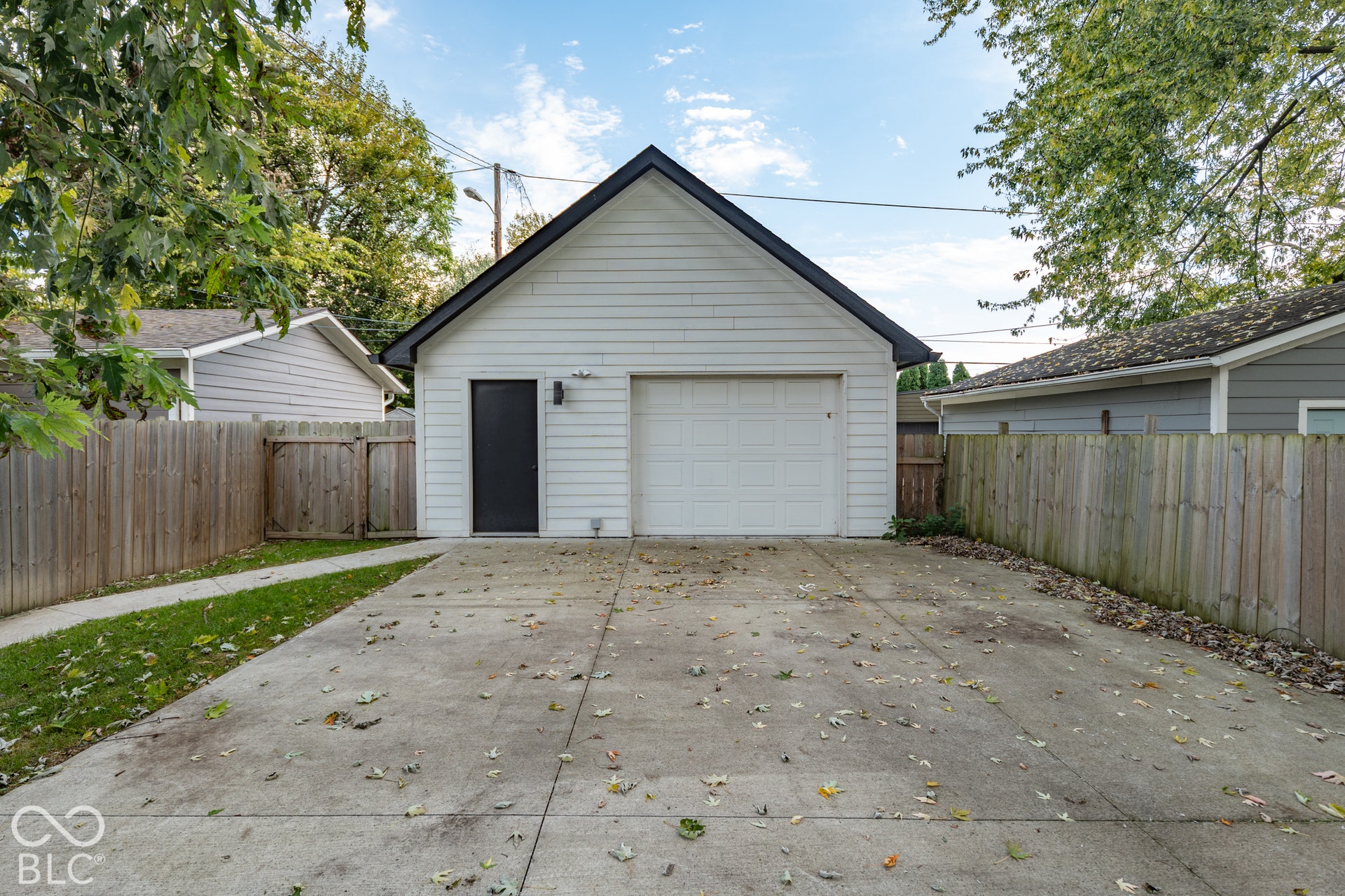 1401 Olive Street, Indianapolis, IN 46203 Detached garage featuring white horizontal siding, a gabled roofline, a single-car garage door, and an exterior side entry door, complete with a concrete driveway