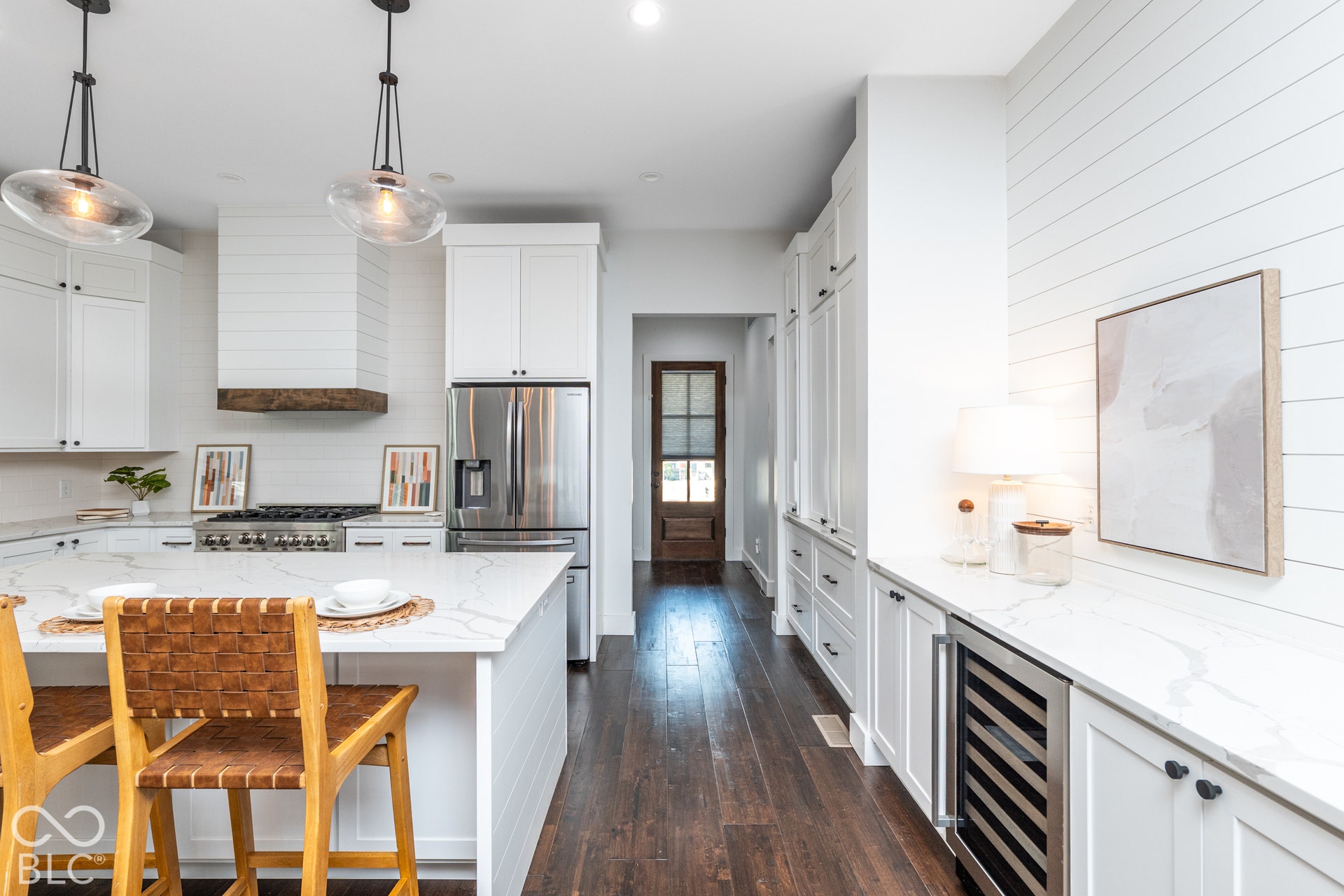 1401 Olive Street, Indianapolis, IN 46203 Kitchen featuring white shaker-style cabinetry, an oversized island with stone-finish countertops, shiplap wall detailing, wood-finish flooring, and a built-in beverage refrigerator