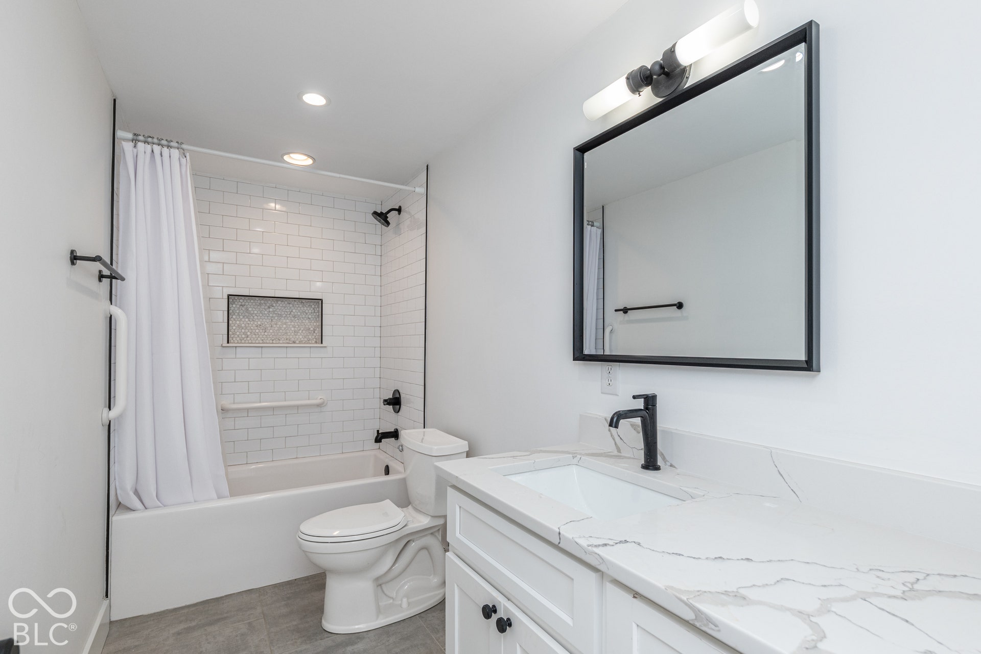 1401 Olive Street, Indianapolis, IN 46203 White vanity with a veined stone-finish countertop, undermount sink, matte black faucet, subway tile shower surround with a built-in niche, and a rectangular mirror with a matte black frame