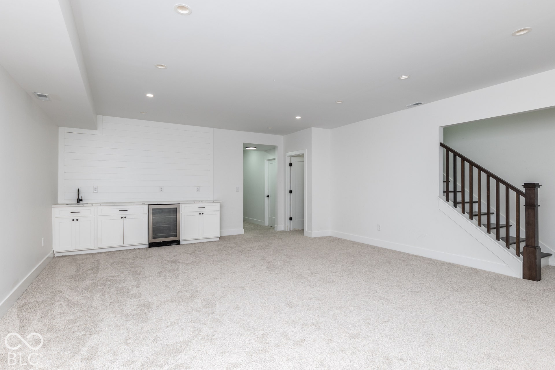 1401 Olive Street, Indianapolis, IN 46203 Open floor plan featuring recessed lighting, a wet bar with shaker-style cabinetry and a beverage refrigerator, shiplap wall accent, and a staircase with a stained wood handrail