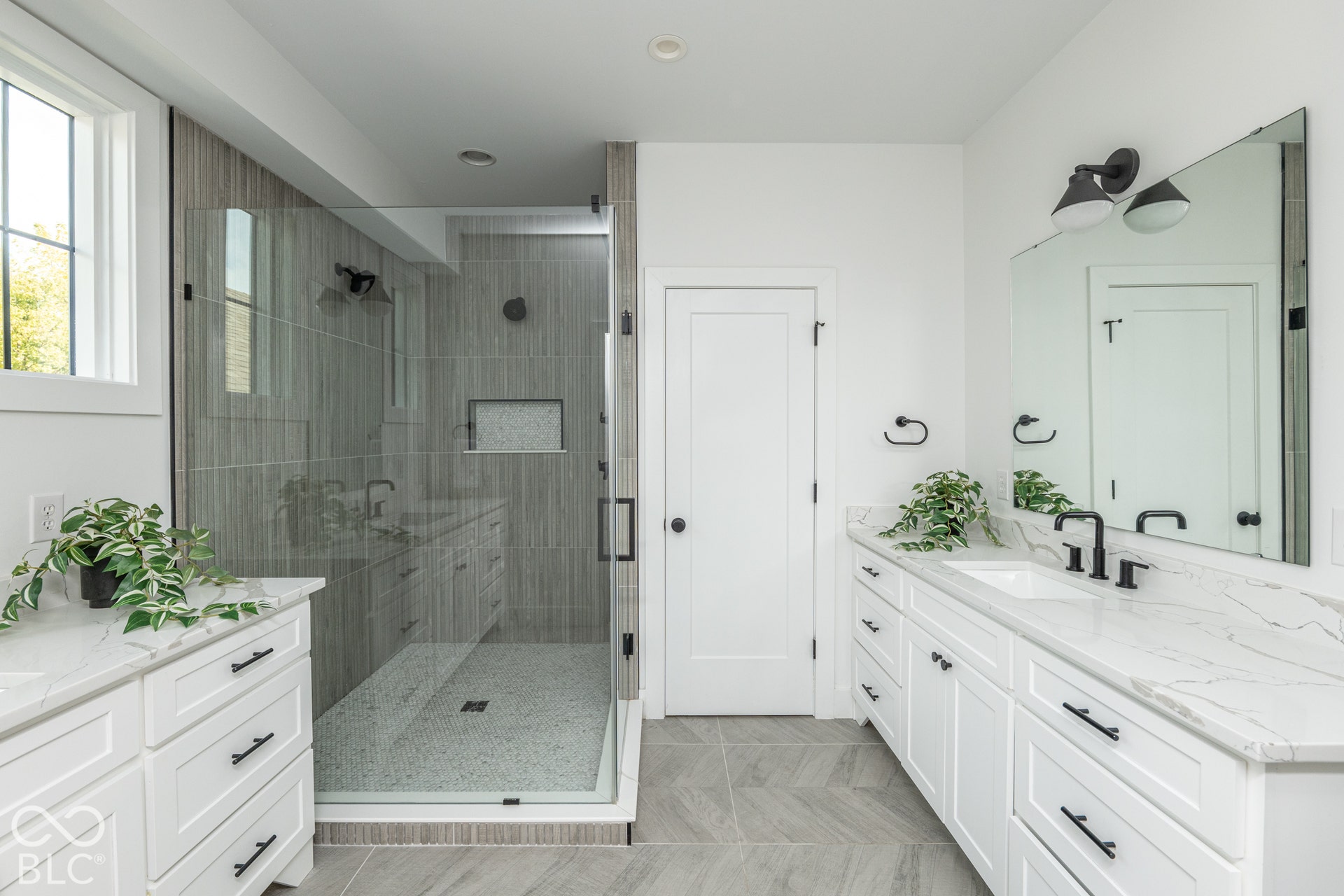 1401 Olive Street, Indianapolis, IN 46203 Dual vanity with white cabinetry and stone countertops, glass-enclosed shower with tiled walls and built-in niche, and herringbone-patterned tile flooring