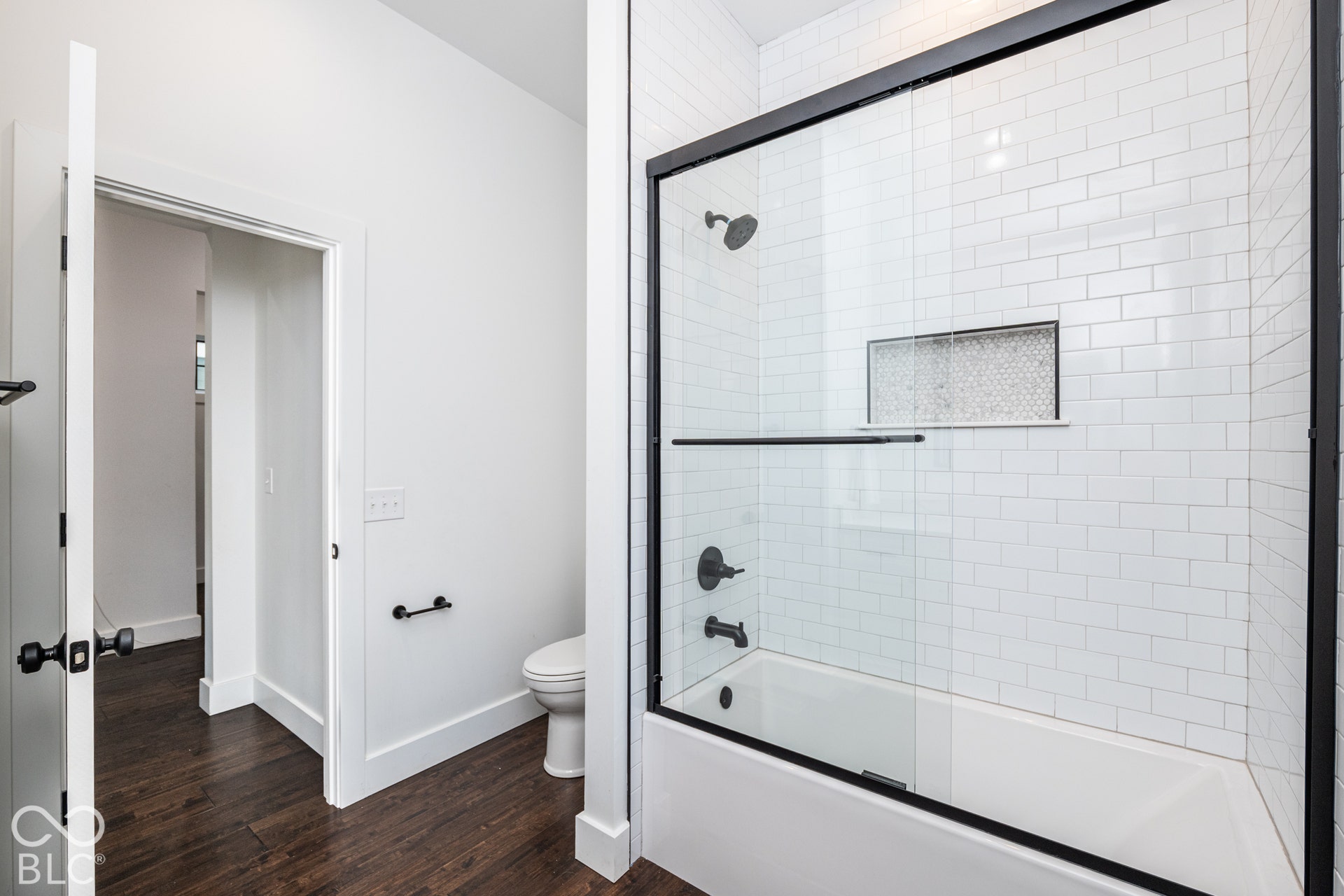 1401 Olive Street, Indianapolis, IN 46203 Bathtub with white subway tile surround, integrated mosaic-tiled shower niche, glass shower door with matte black hardware, and dark wood-finish flooring