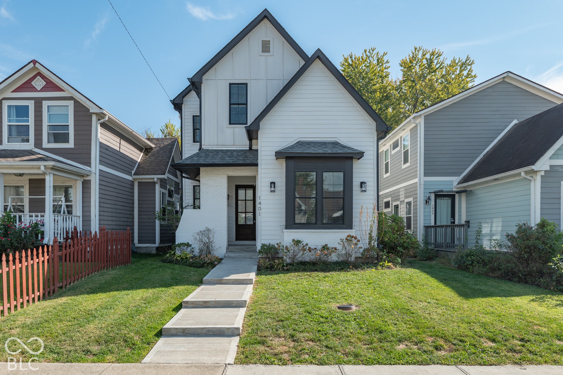 1401 Olive Street, Indianapolis, IN 46203 Two-story farmhouse exterior featuring white board-and-batten siding, a brick facade entryway, a front-facing bay window, and dark window trim