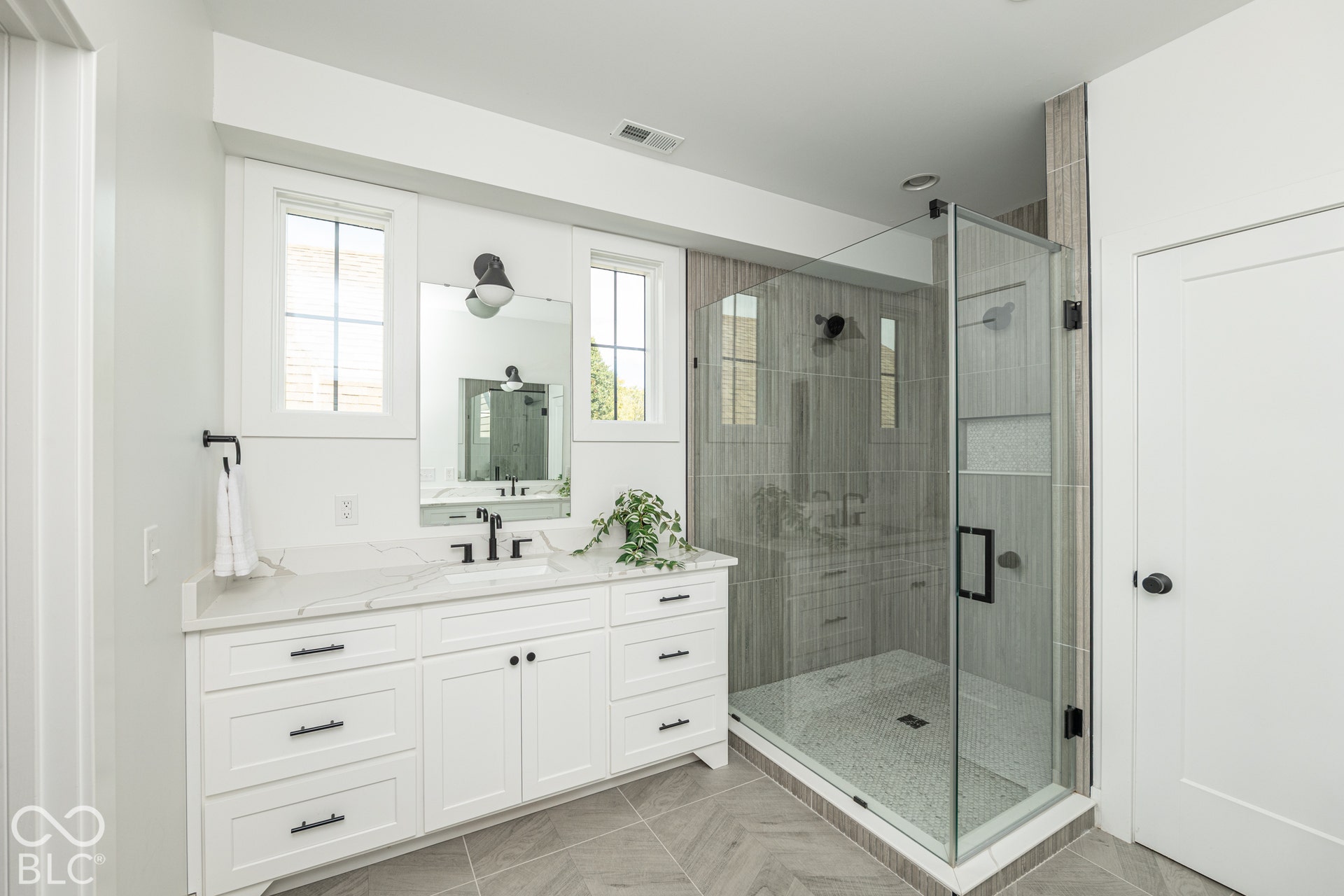 1401 Olive Street, Indianapolis, IN 46203 White vanity cabinet featuring a stone countertop, integrated sink, and matte black hardware, paired with a glass-enclosed shower featuring floor-to-ceiling tile, a built-in recessed shelf, and gray chevron-patterned tile flooring