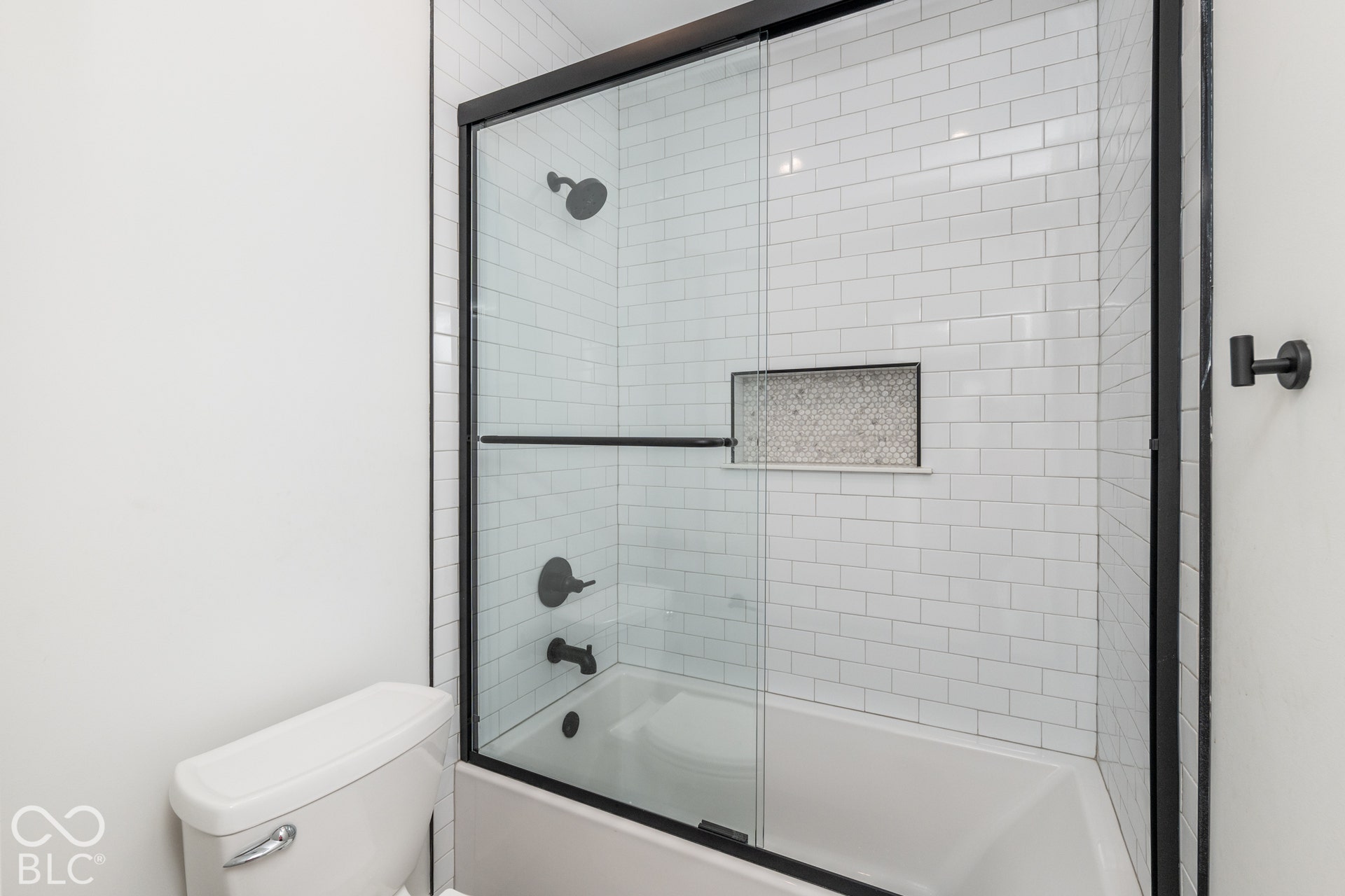1401 Olive Street, Indianapolis, IN 46203 Bathtub with white subway tile surround, integrated mosaic tile recessed niche, matte black shower fixtures, and a sliding glass door