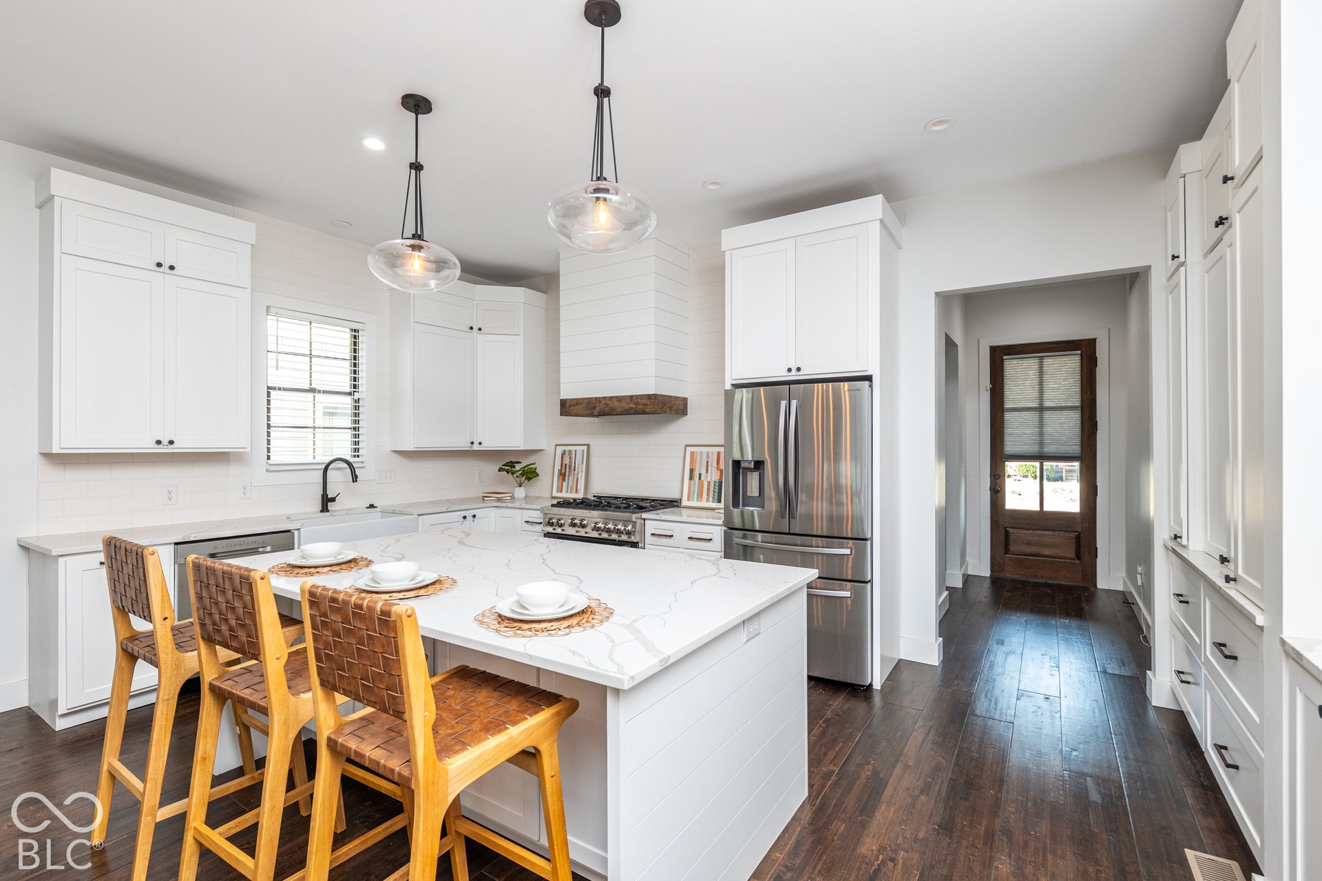 1401 Olive Street, Indianapolis, IN 46203 Kitchen featuring white shaker cabinetry, an oversized quartz-topped island, wood-finish flooring, stainless steel appliances, and a custom range hood