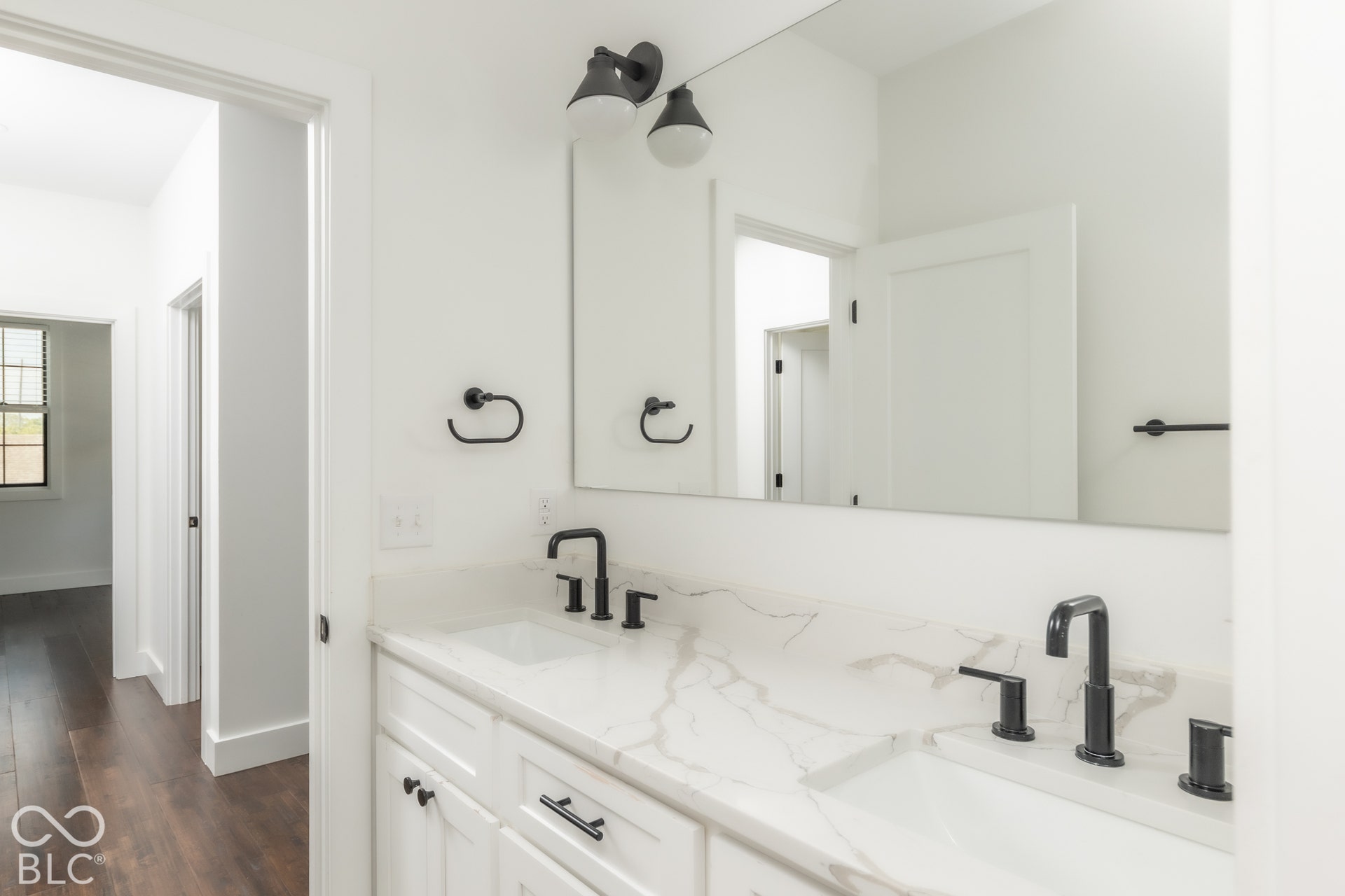 1401 Olive Street, Indianapolis, IN 46203 Dual-vanity cabinet with stone-finish countertop, undermount sinks, matte black widespread faucets, large wall-mounted mirror, and industrial-style dual-bulb lighting