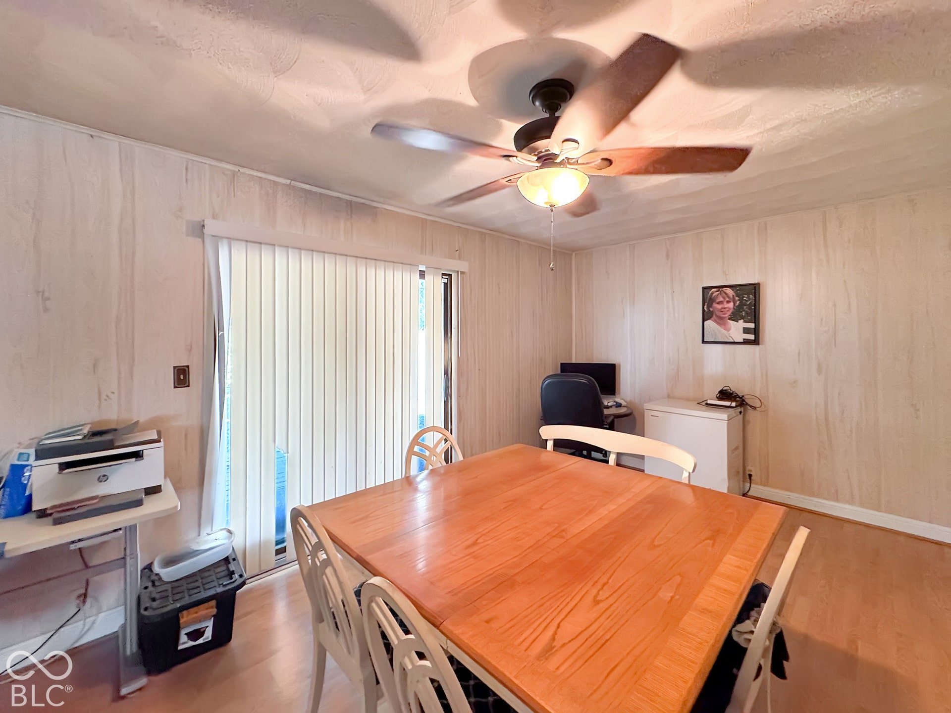 Spacious dining area featuring warm wood-finish flooring, wood-paneled walls, and a ceiling fan with integrated lighting
