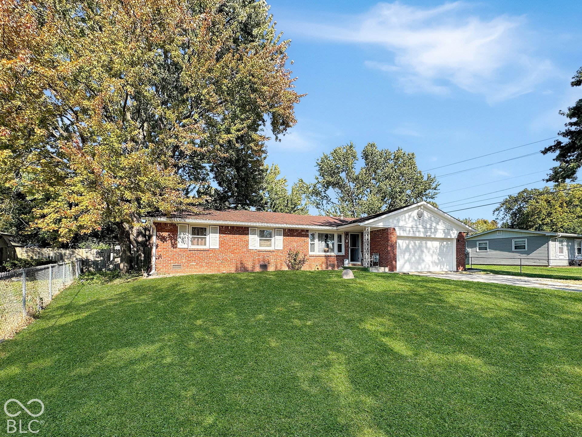 Virtually Altered - Brick exterior featuring white shutters, an attached two-car garage, and mature trees on a level lawn