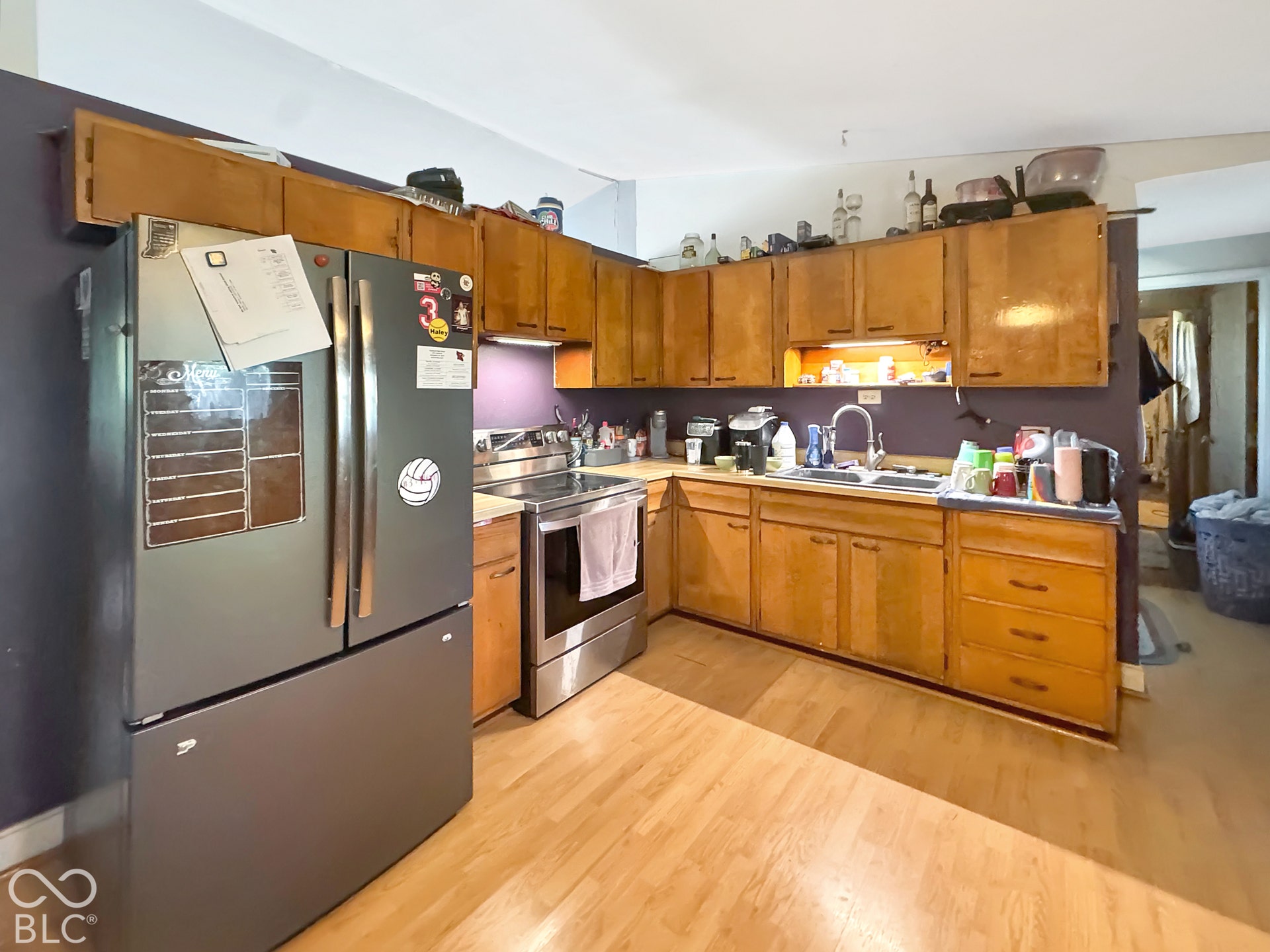 Kitchen featuring wood cabinetry, stainless steel refrigerator and range, wood-finish flooring, and a dual-basin sink with a gooseneck faucet