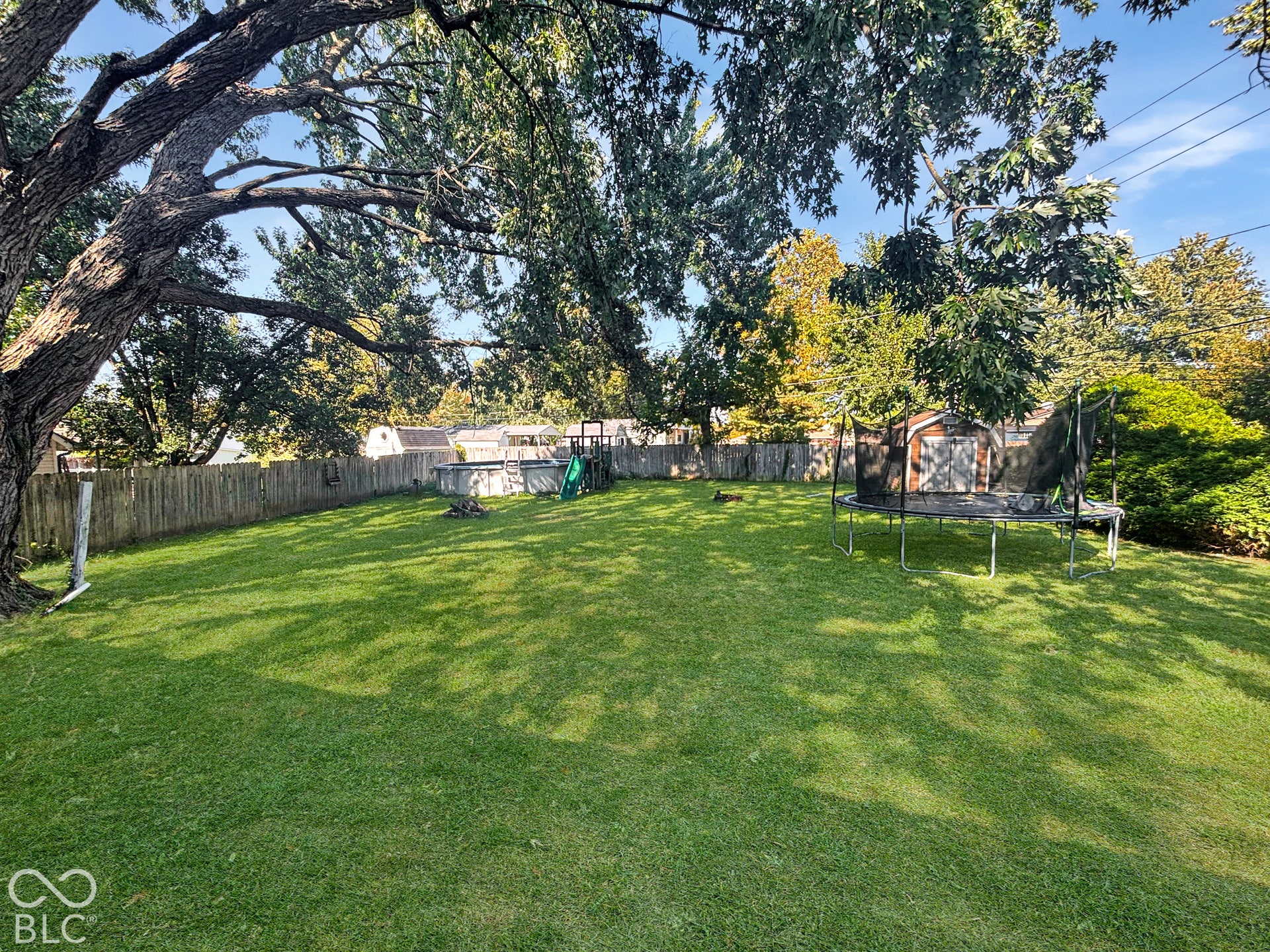 Virtually Altered - Expansive backyard featuring a large grass lawn, mature trees, and wooden perimeter fencing