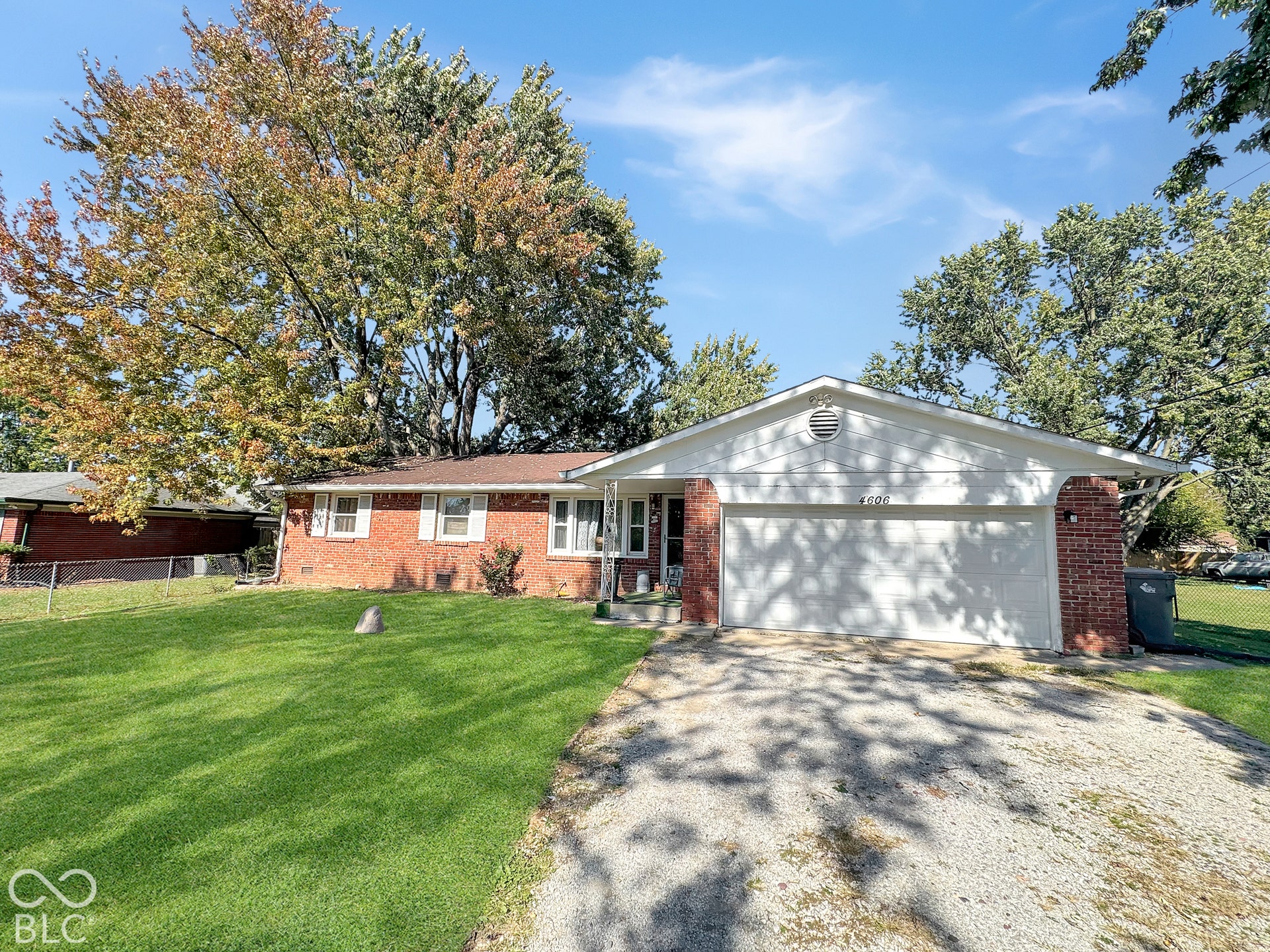 Virtually Altered - Single-story residence featuring a classic red brick exterior, attached two-car garage, and expansive front lawn with mature trees